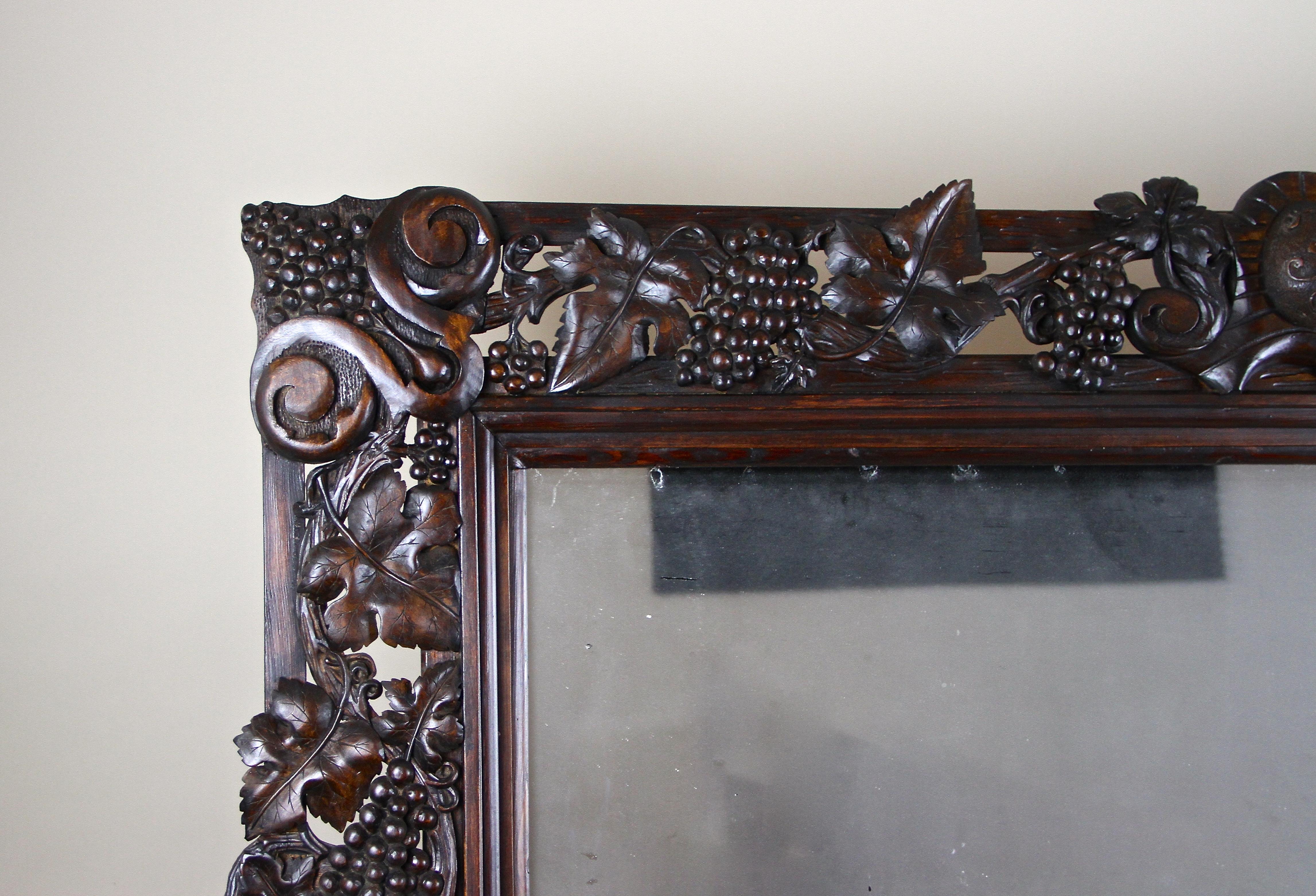Gigantic, one of a kind Black Forest wall mirror out of Austria, dated to 1919. This early 20th century elaborately hand carved masterpiece impresses with a fantastic open worked vine theme, showing artfully carved grapevines with grapes and very