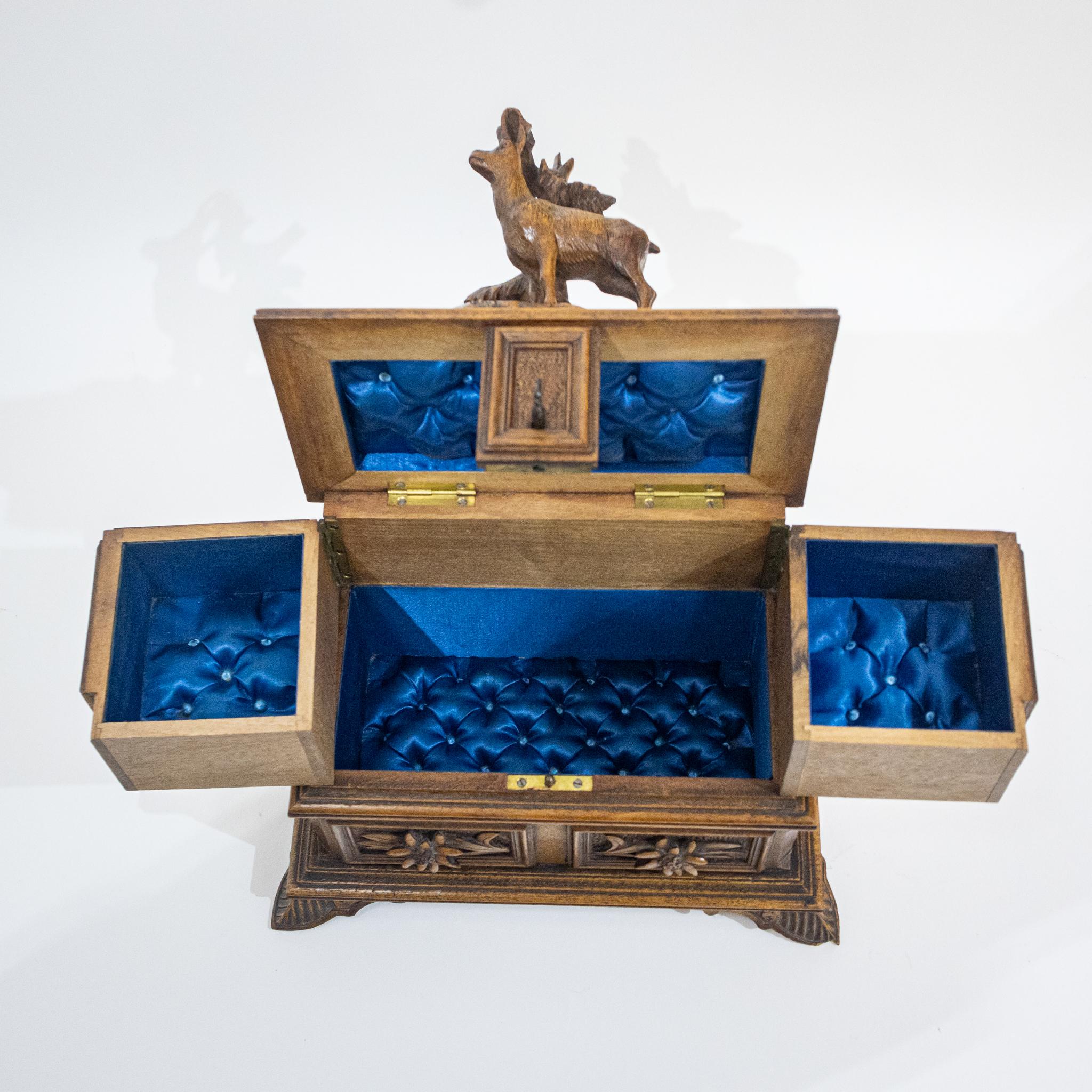 This exquisite early 20th Century Black Forest walnut jewellery box is a true testament to the craftsmanship of its time. Its exterior features intricate carvings of a graceful Chamois goat surrounded by delicate Edelweiss flowers, evoking the charm