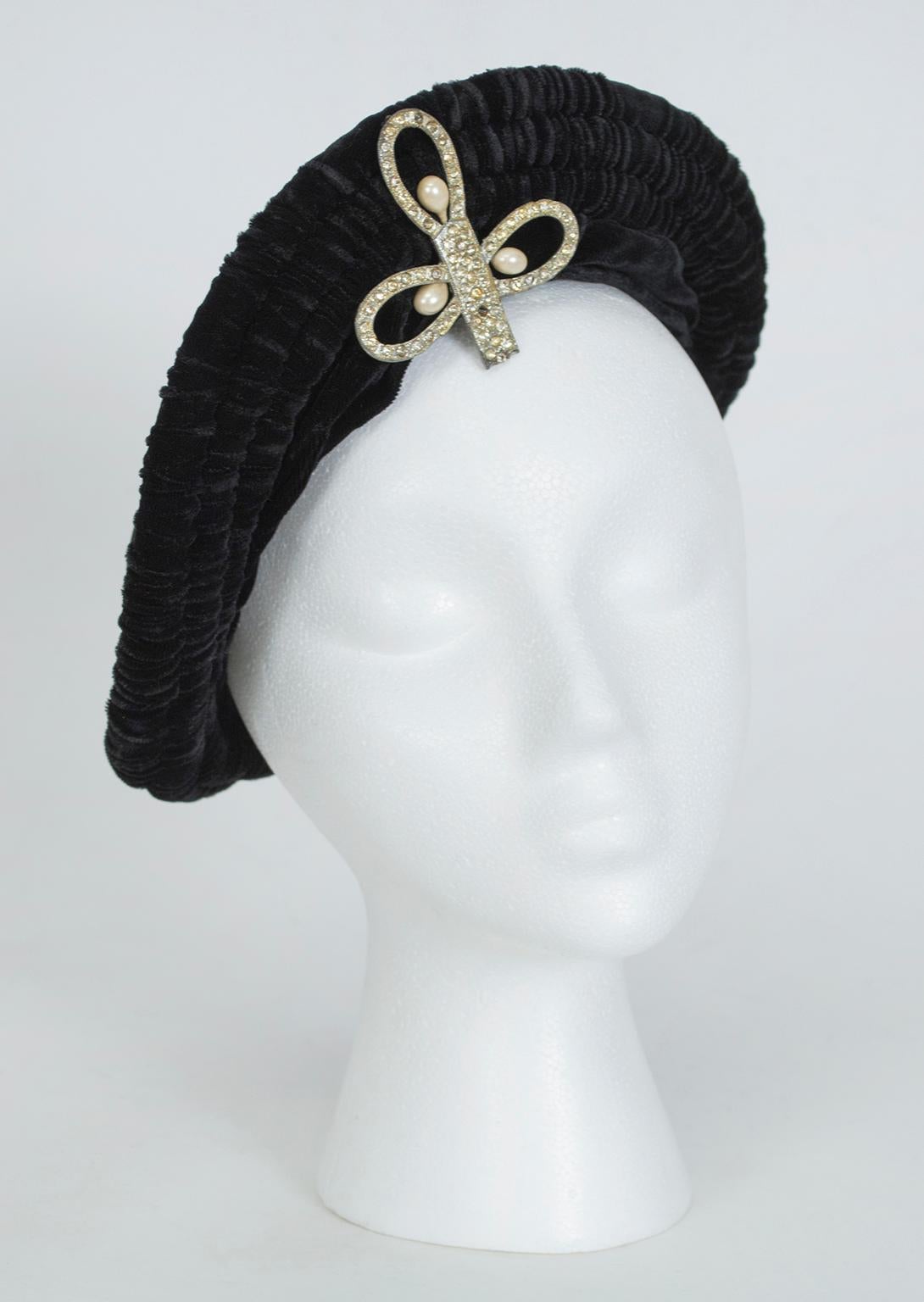 A hat with the regal bearing of a crown, this beret features a massive rhinestone center brooch and lends a royal touch to basic black formalwear.

Pliable silk velvet beret with rolled and gathered edge and 2” self surplice headband around front