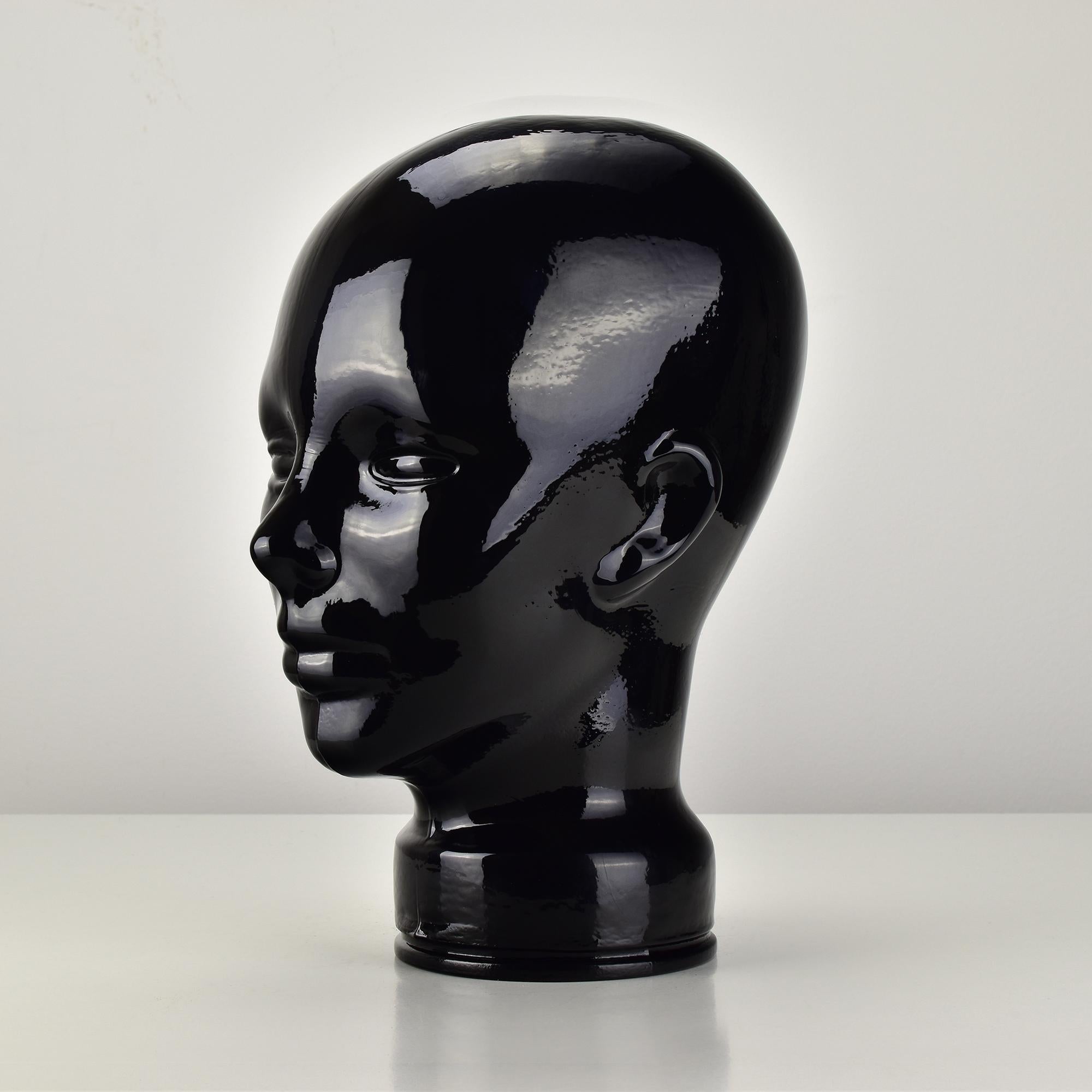 This life-size black glass head sculpture exudes a sleek and striking aesthetic, crafted in Germany during the 1970s. Its glossy finish enhances the deep black hue, creating a bold statement piece ideal for interior decor. Perfect for use as a