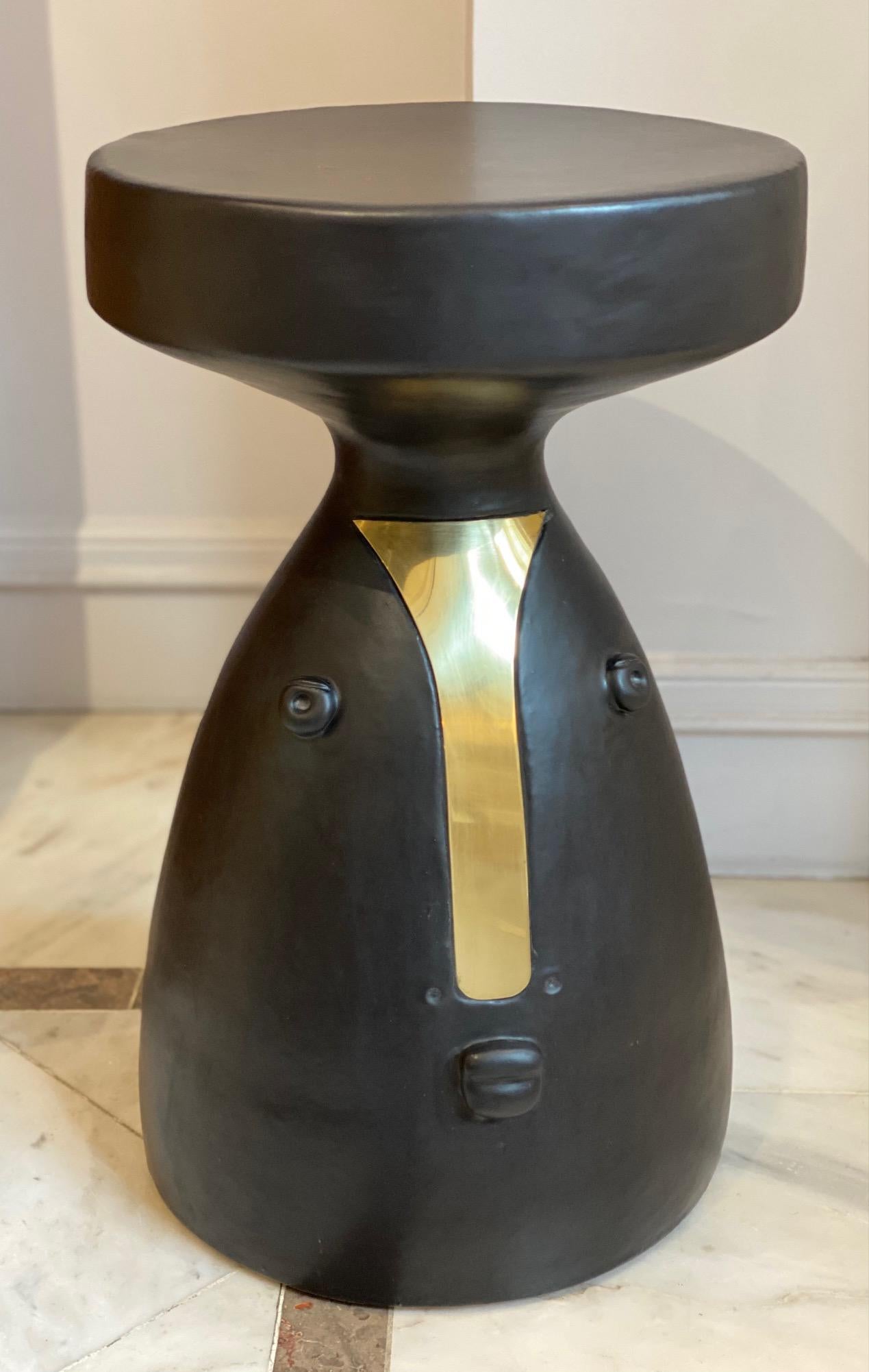 Earthenware black glazed stool (or side table) with stylized face and brass noze 2022.
Unique hand-sculpted piece signed by the French ceramicists DALO.