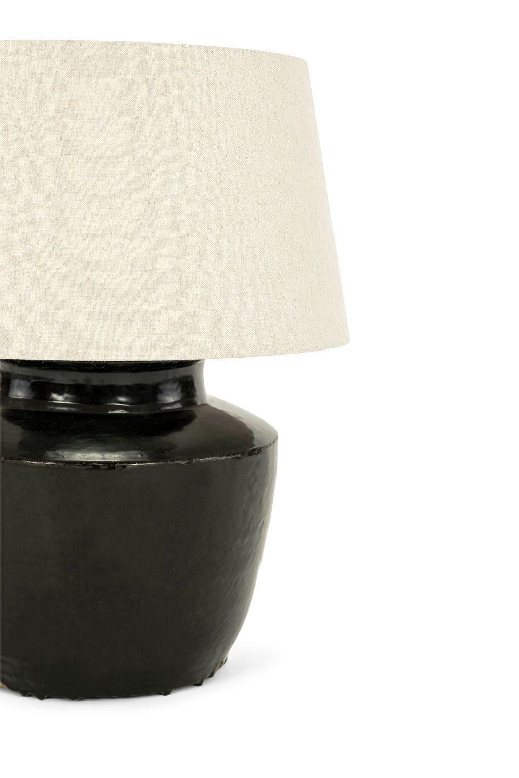 Black glazed terracotta lamp, newly wired for use within the USA with line switch. Includes off-white linen drum European uno shade (listed measurements include shade).