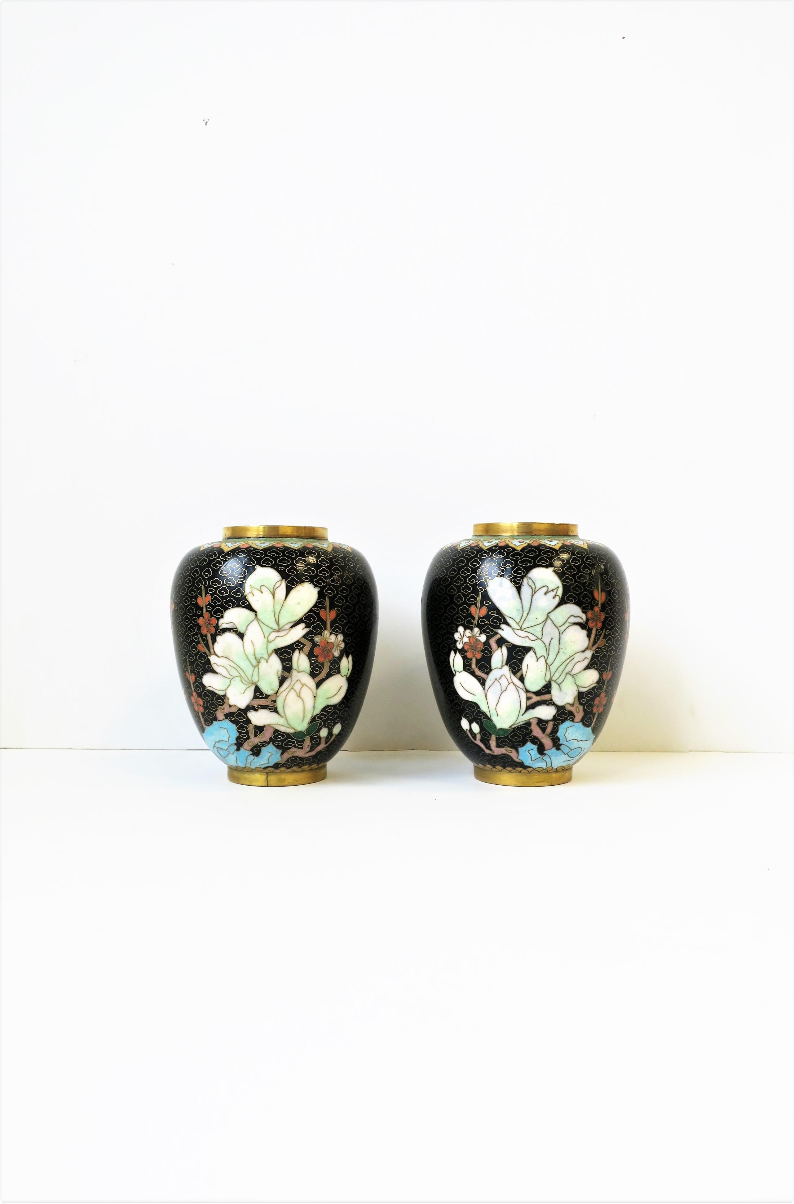A very beautiful pair of vintage Asian black and pastel color enamel cloisonné´ and brass vases, circa 20th century, Asia. Beautiful, detailed design of flowers; Larger flowers on front, smaller cherry blossoms on sides, and spider chrysanthemums on