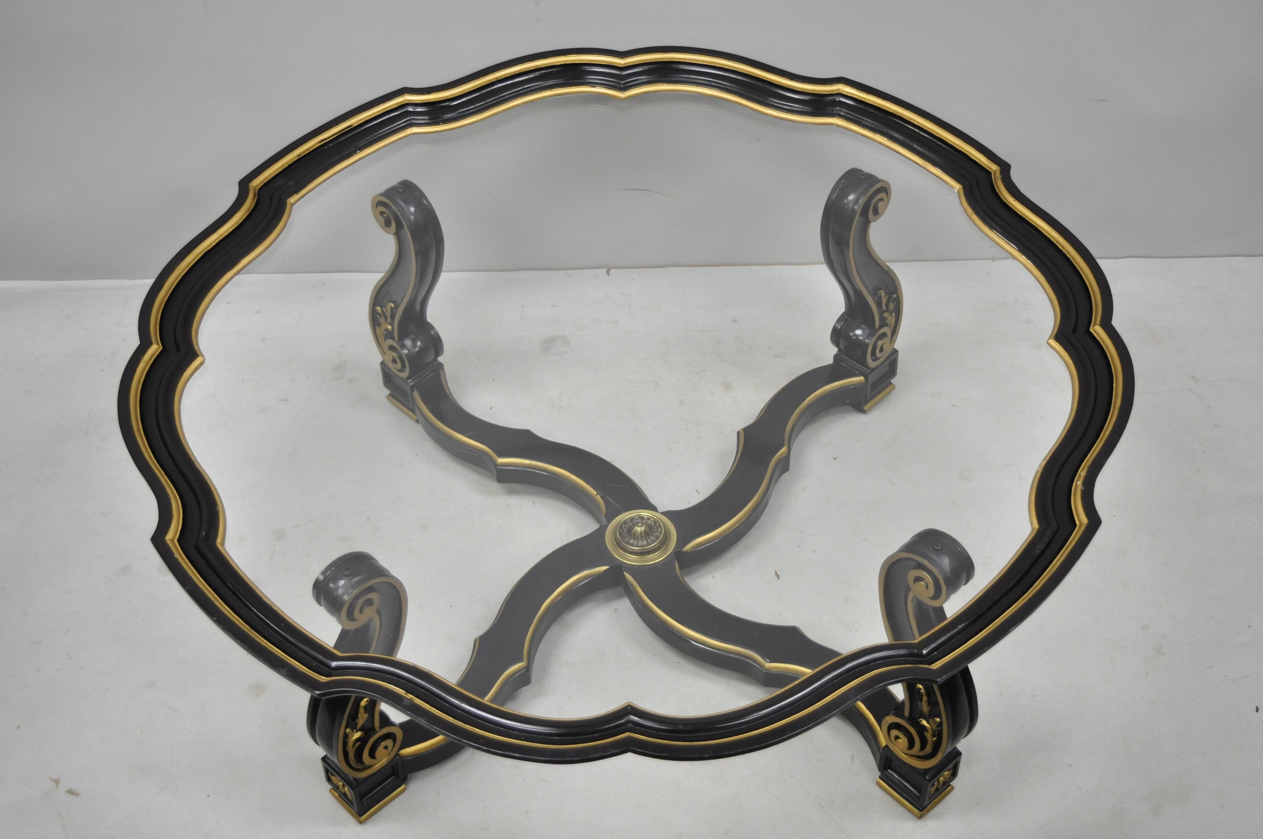Vintage black and gold French style Hollywood Regency tray coffee table with scalloped edge. Item features black and gold painted finish, carved base, glass top, shaped border, brass finial, great style and form, circa mid-20th century.
