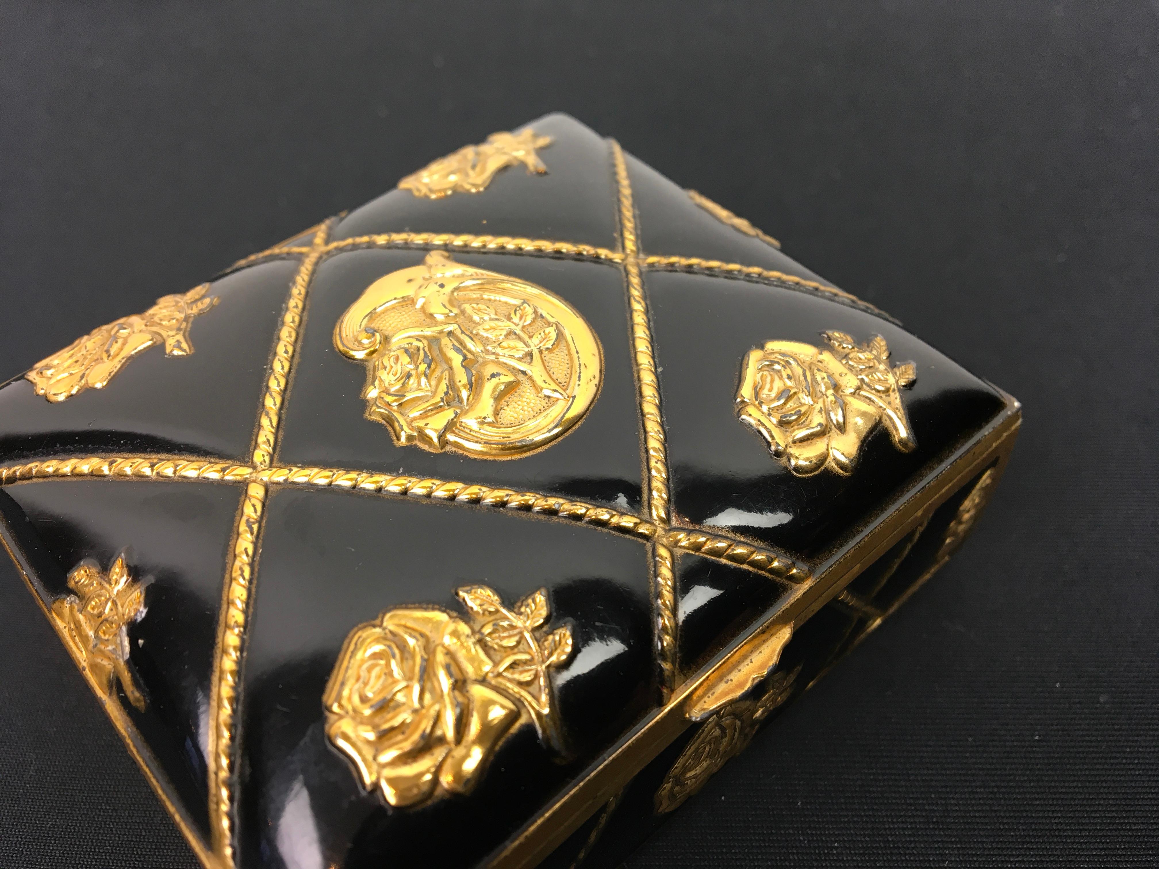 Black and gold jewelry box with roses.
This stylish trinket box has as basis color black with embossed gold roses and lines in the shape of cords. 
Inside this little storage box with lid is red velvet and under you find 4 invisible legs. 

It's
