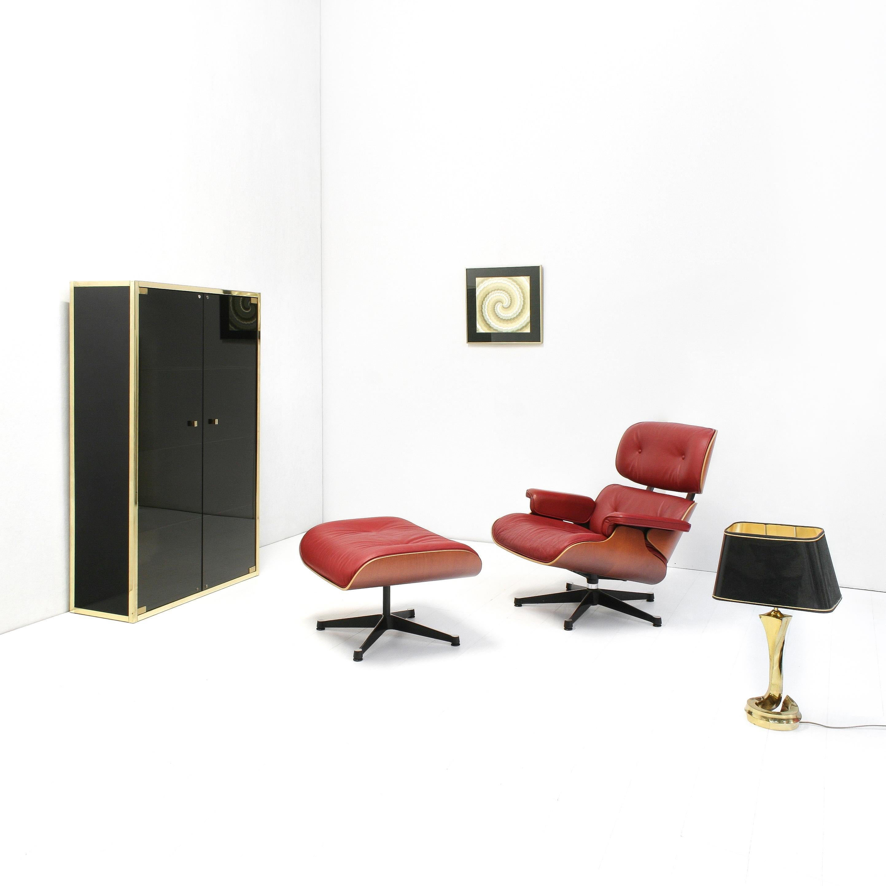 Ce meuble à étagères élégant a été créé dans les années 1970. Il se compose d'un boîtier laqué noir brillant, entouré de bords dorés et de portes et étagères en verre fumé.