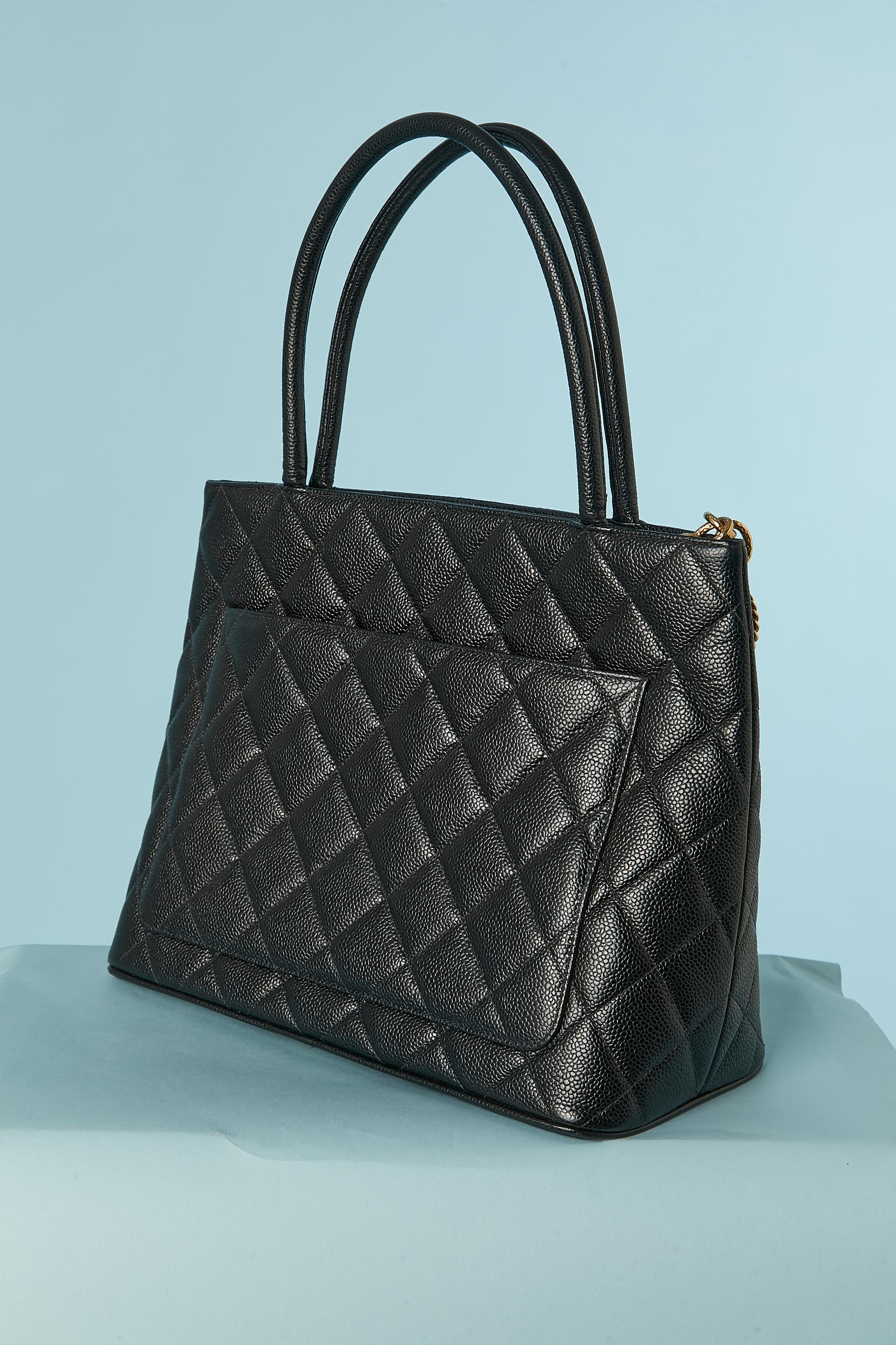 Black grained leather top handle back with top-stitching. Black leather lining. Zip closure on the top middle with gold chain and 