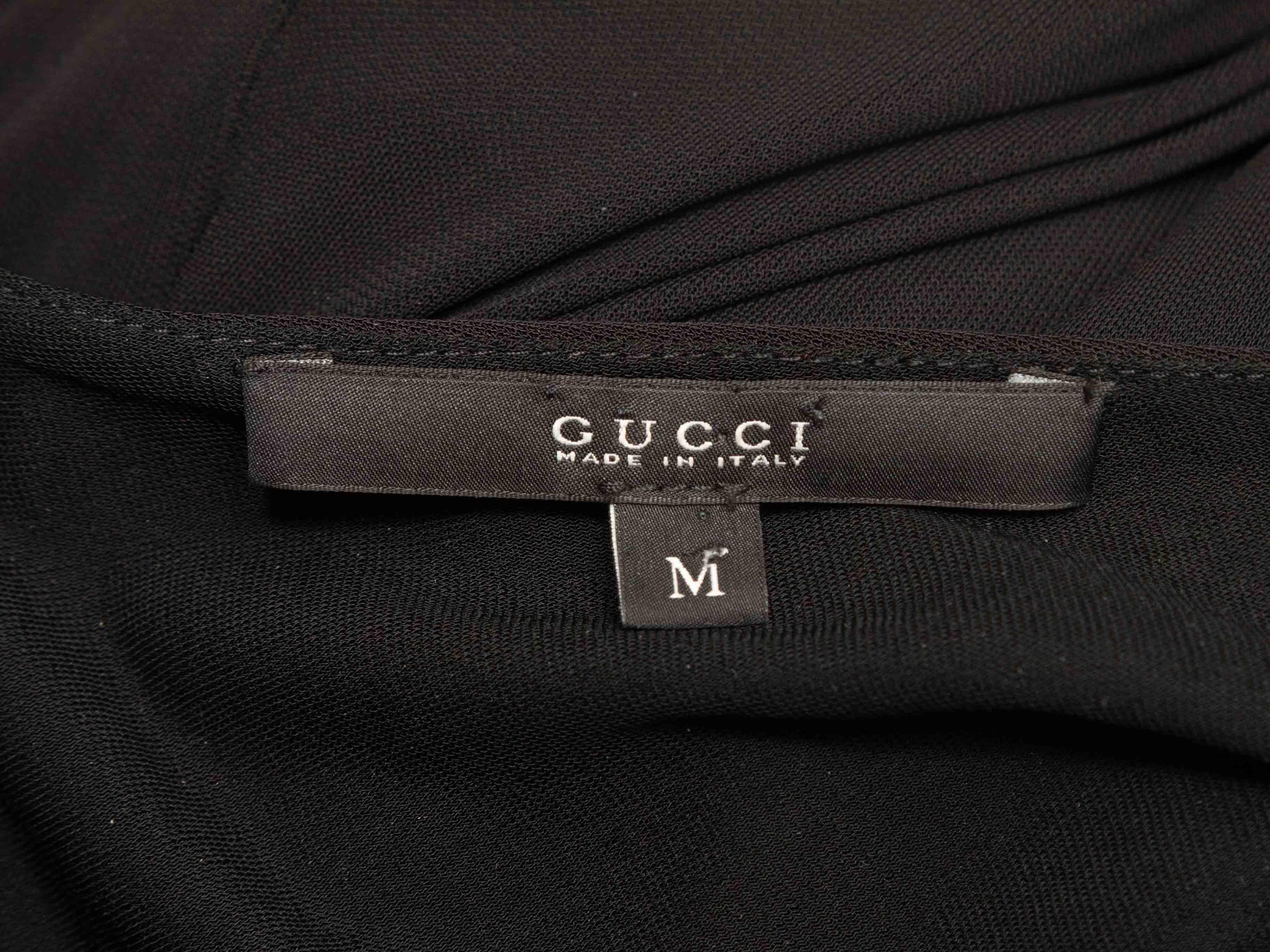 Robe noire ruchée à manches longues et longueur au genou, signée Gucci. Encolure en V, avec des accessoires en métal doré. Fermeture à glissière au dos. Poitrine 28