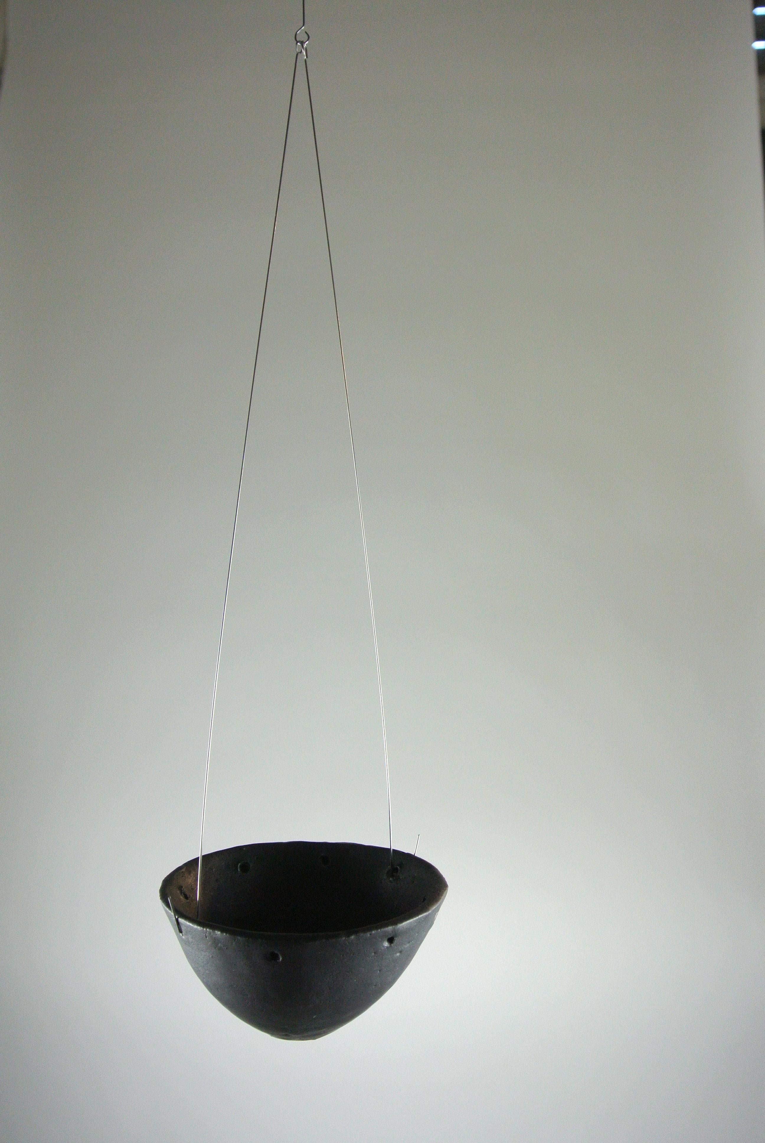 Hand build black stoneware candleholder with black matte glaze. Slightly asymmetric shape and small holes divided out around the top edge to adjust hanging position.
Hangs from ceiling from thin metal rod. Available with hard ware upon