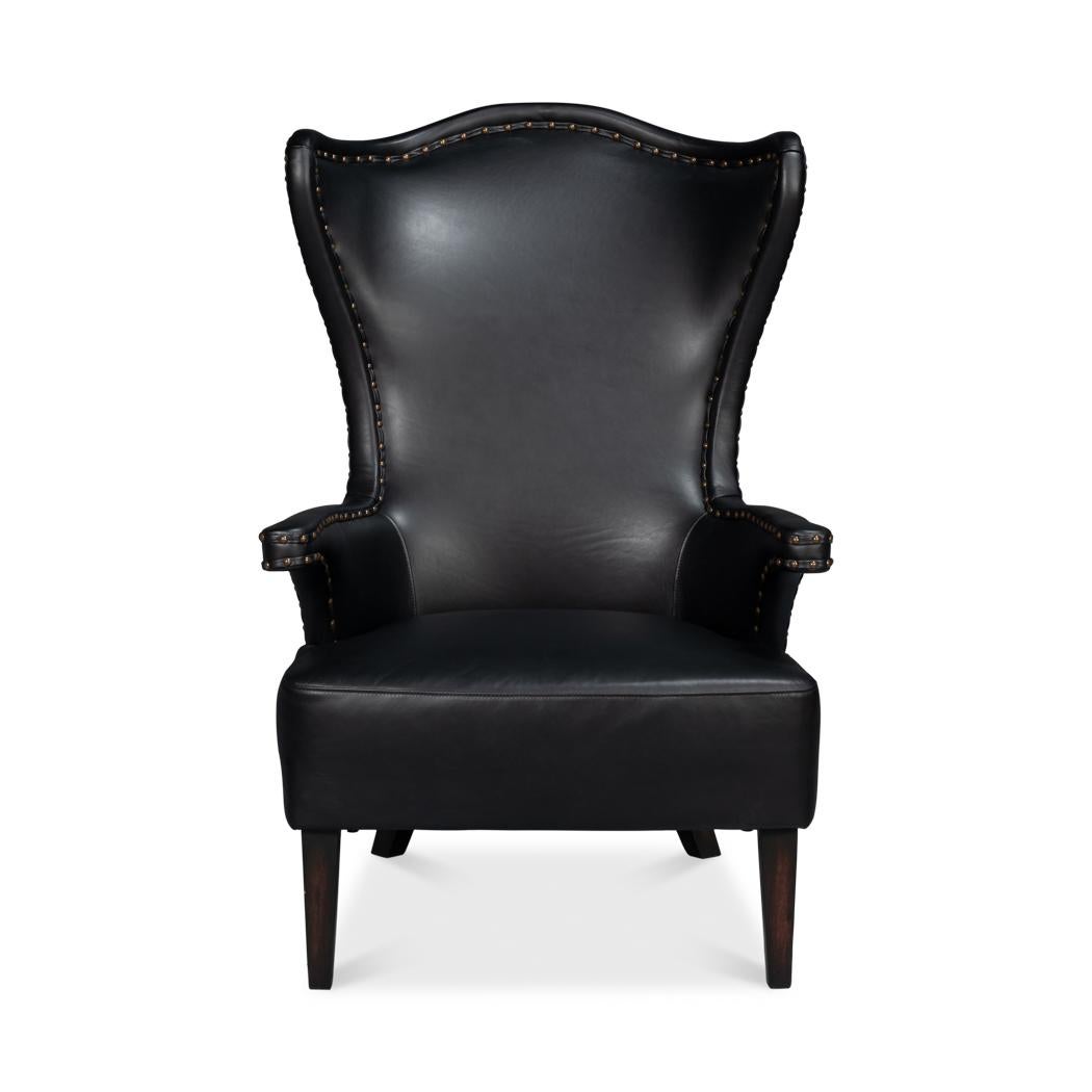 Upholstered in rich, full-grain onyx black leather, this chair features a dramatic high-back design that creates an elegant silhouette. The winged sides and gently curved arms are accentuated with meticulous nailhead trim, adding a refined touch of