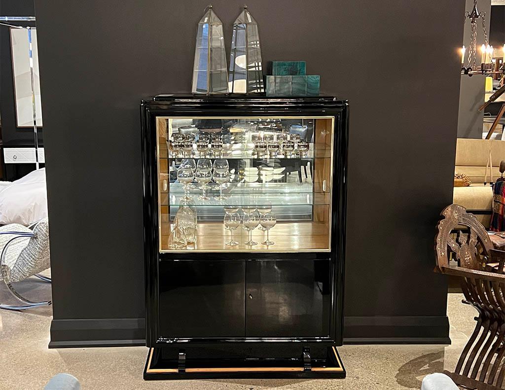 Black high gloss Art Deco cabinet. Stunning French Art Deco styling, featuring high gloss polished black lacquered finish with brass metal inlay. Sliding glass doors reveal the large display area with mirrored back and 2 glass shelves. Bottom of the