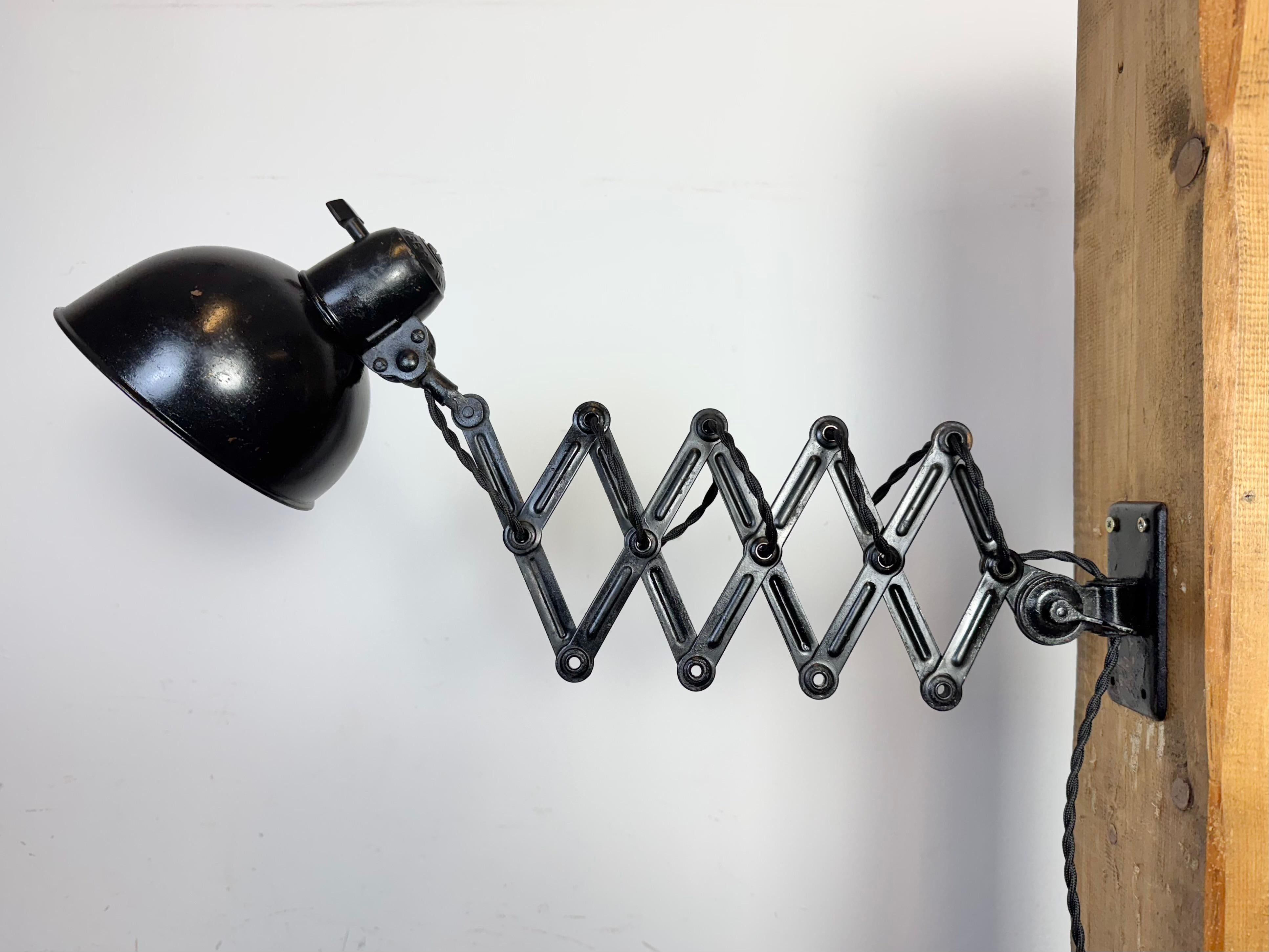 Aplique de tijera industrial regulable Bauhaus diseñado por Christian Dell y fabricado por Kaiser Idell en Alemania durante la década de 1930. Es de metal pintado de negro. El brazo de tijera de hierro es extensible y puede girarse lateralmente. El