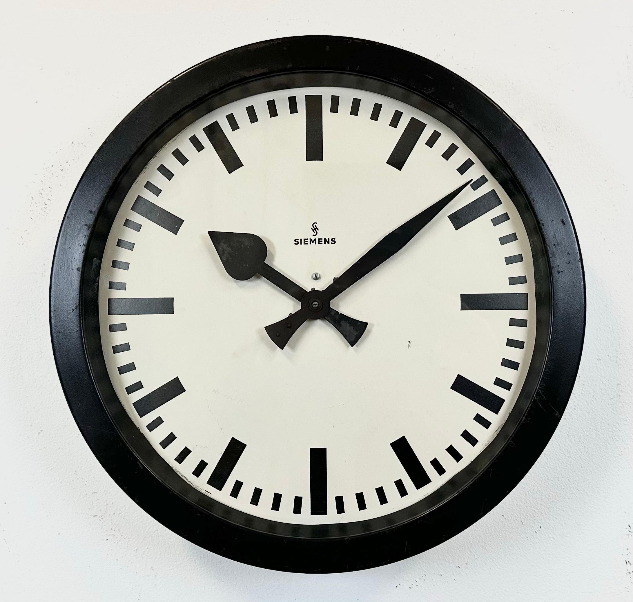 This wall clock was produced by Siemens in Germany during the 1950s. It features a black metal frame, a metal dial and a clear glass cover. The piece has been converted into a battery-powered clockwork and requires only one AA-battery. The weight of