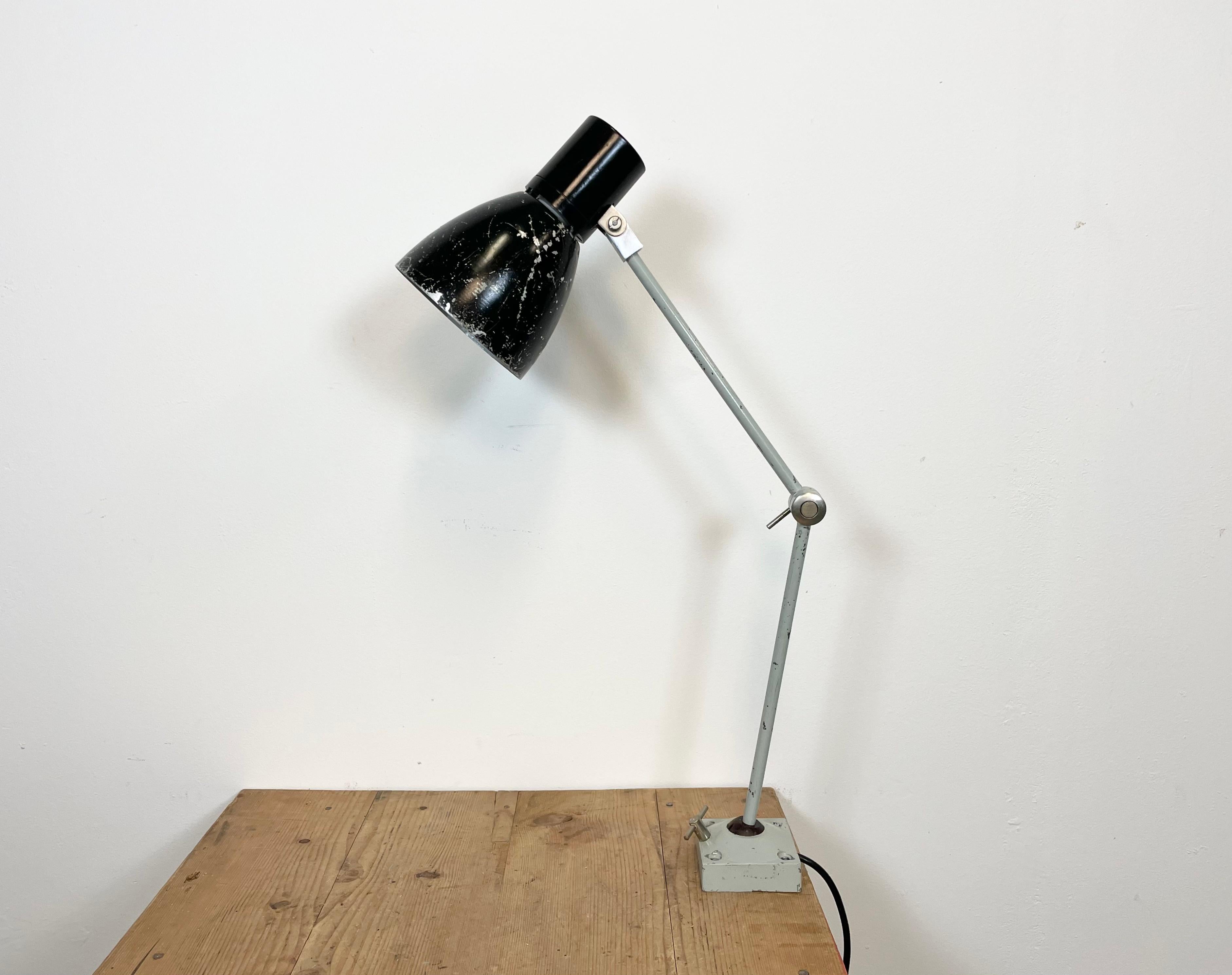 Lámpara de mesa industrial fabricada por Elektrosvit en la antigua Checoslovaquia durante la década de 1970. Tiene una base y un brazo de hierro gris con tres articulaciones ajustables y una pantalla de aluminio negro con la parte superior de