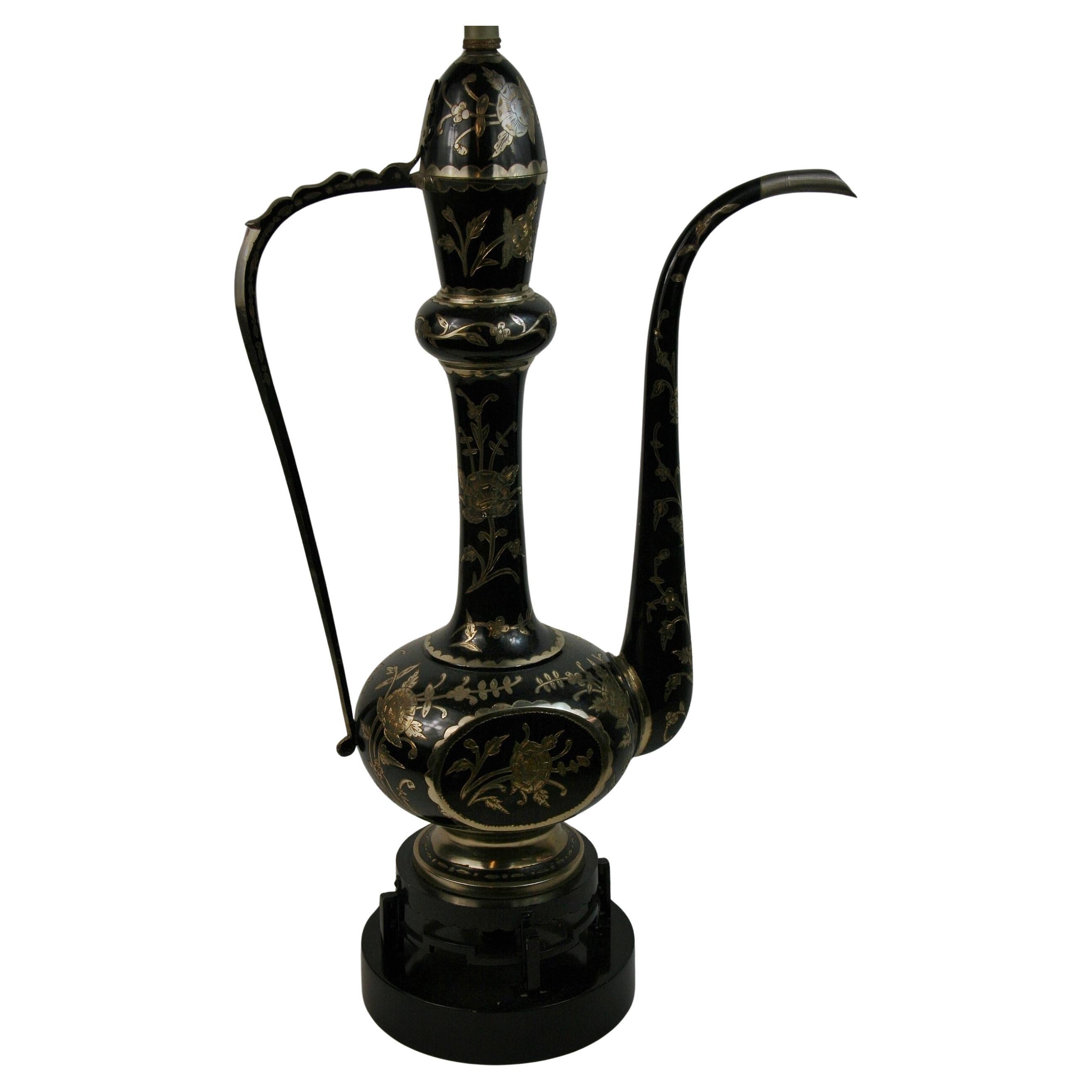 2-298 lampe de table en forme d'aiguière en laiton argenté et émaillé noir. La lampe présente des découpes décoratives dans l'émail noir qui forment des motifs floraux et des feuilles complexes.
Posé sur un double socle en métal et en bois
