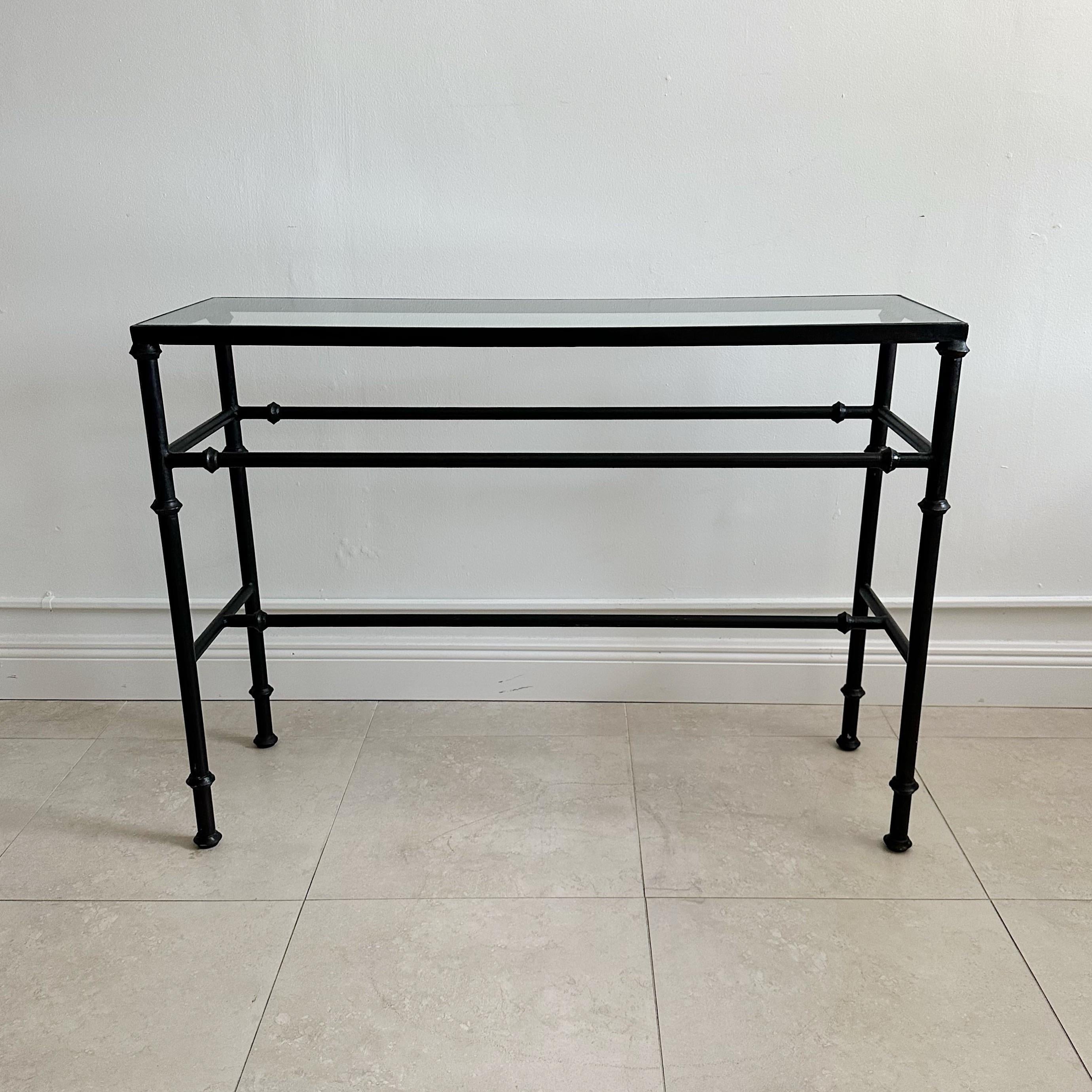 This slender Iron Console Table with inset glass is a sleek and versatile piece, painted in a black finish that makes it suitable for both indoor and outdoor use. Its petite size ensures ease of placement and utilization. The design of the table is