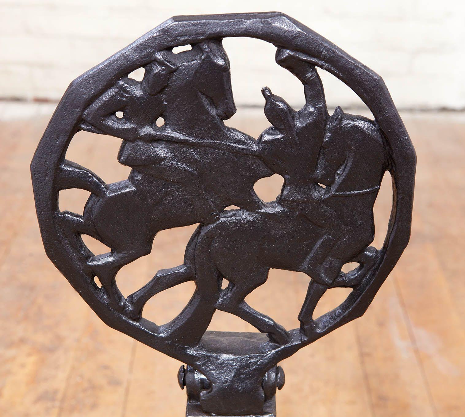 A pair of heavy gauge black wrought iron Art Deco andirons. Unique design having roundels with horsemen filigree casting inside dodecagon (12 sided) surrounds on tapering shafts over arched legs with distinctive sunburst decoration. One andiron with