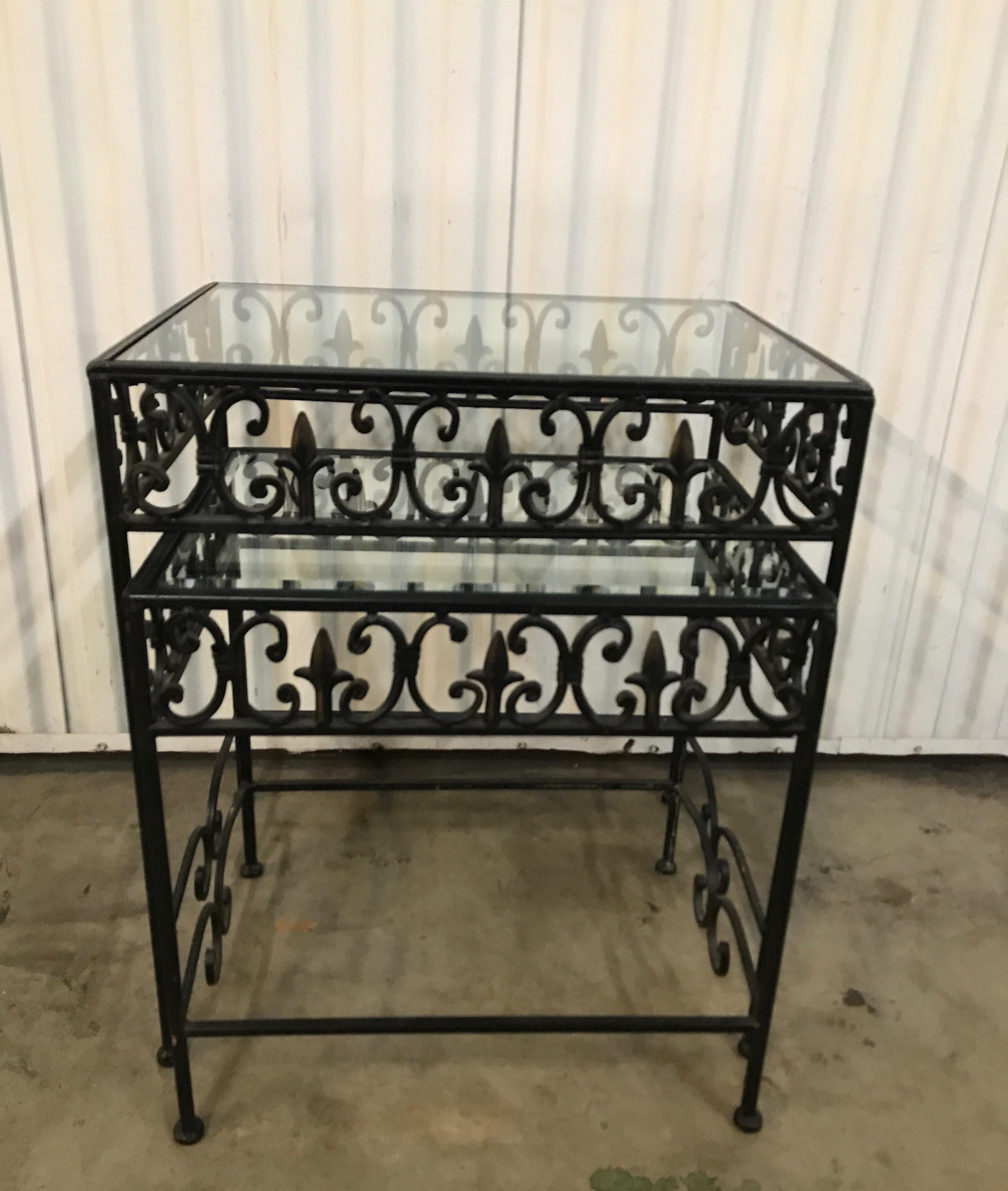 Fleur de lys black iron stacking tables with glass tops.