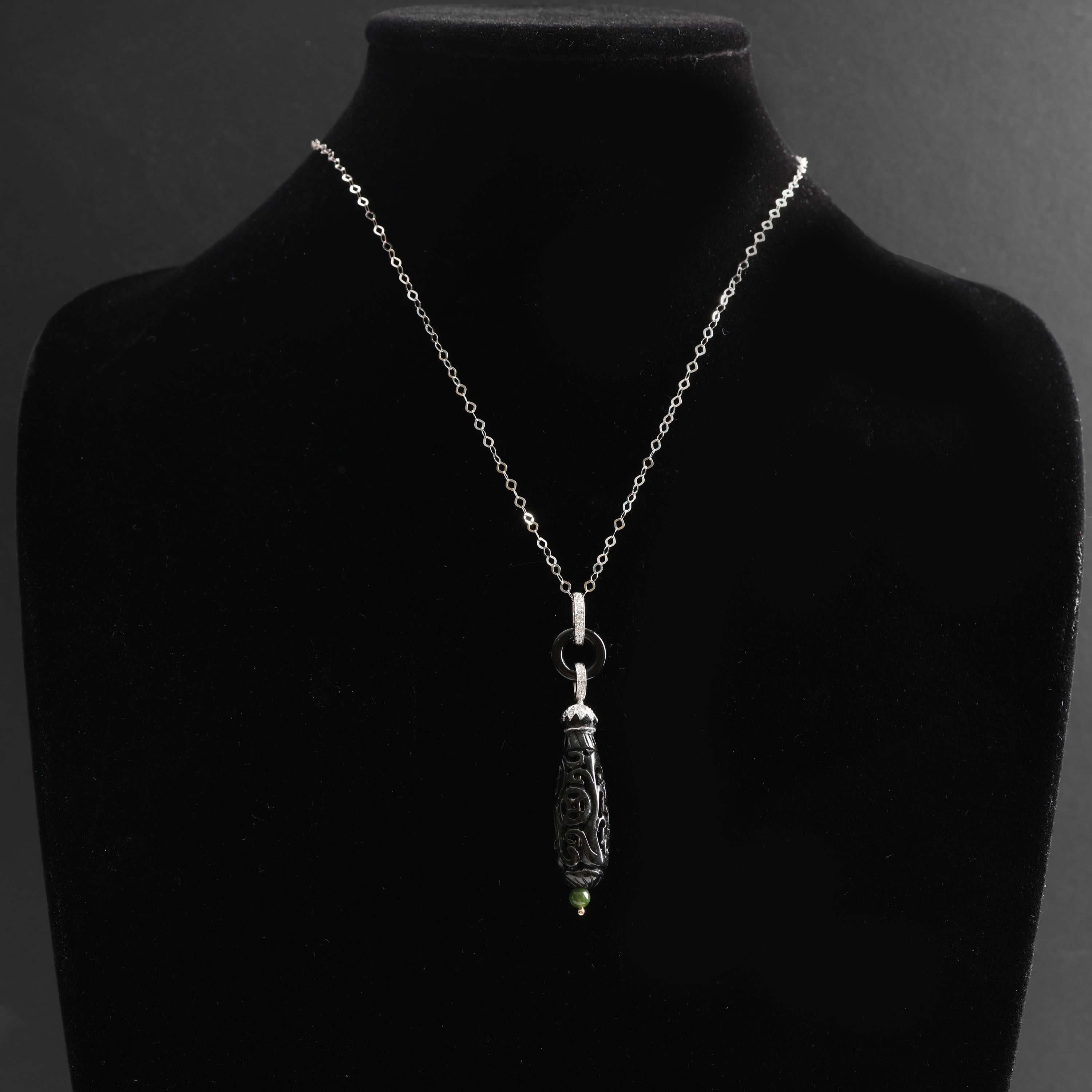 A dramatic hand-carved and highly detailed black nephrite jade drop that measures approximately 35mm x 11mm is suspended from an Art Deco style bail in 14K white gold. The bail features numerous tiny white diamonds, a 12mm ring of glossy black onyx,