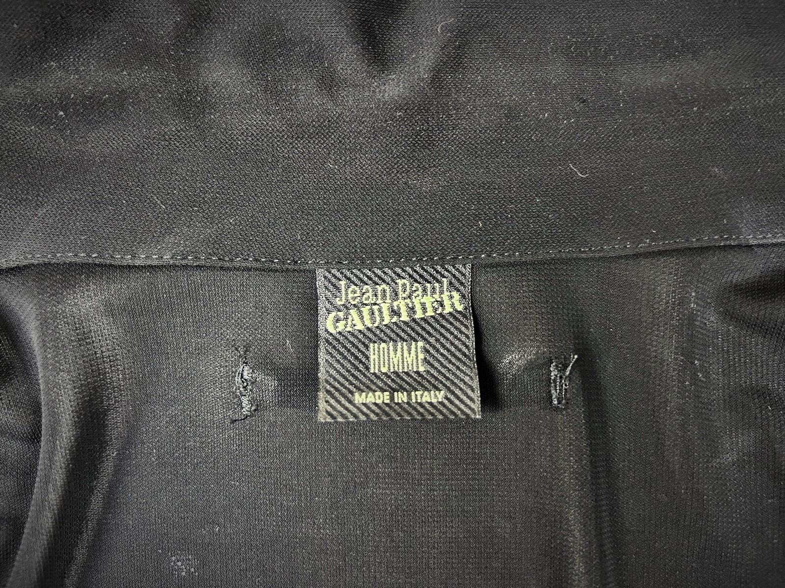 Circa 1995
Francia
Camisa negra semitransparente de punto de acetato elástico de Jean Paul Gaultier Homme de los años 90. Corte entallado, mangas largas con cuello en punta, bolsillo y puños perforados y decorados con cadenas de metal con