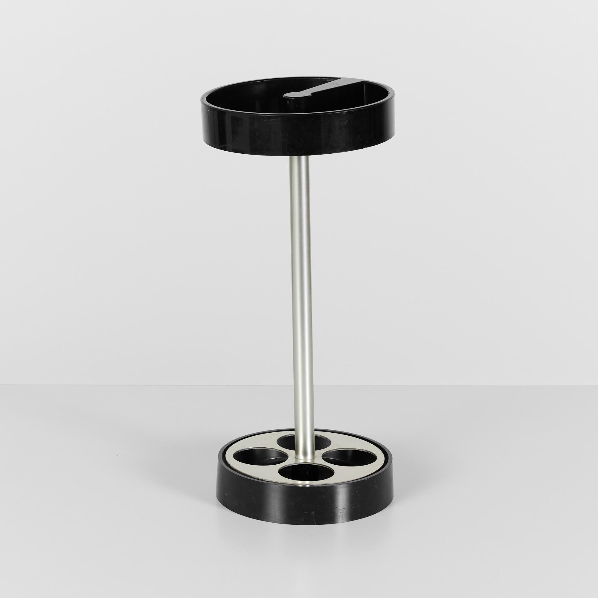 Free standing simplistic barbell design of brushed aluminum and black plastic make up this umbrella stand from Italian design house Kartell. This stand features a circular pedestal base with round aluminum cutouts to hold up to four umbrellas. The