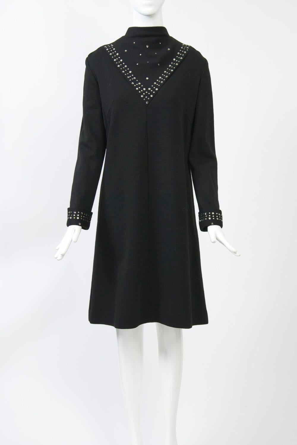 C.I.C. 1970 Robe trapèze en double tricot noir, col cheminée et manches longues avec poignets retournés. Le devant du cou est orné d'un V composé de trois rangées de strass de grande et de petite taille alternant sur les deux rangées extérieures,