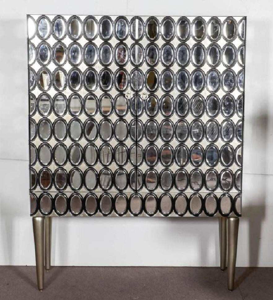 Extravagant and striking black lacquer and silver leaf cabinet with over 200 hand beveled oval mirror insets, raised on tapered silver leaf legs.
Can be used in any setting as a decorative tall cabinet, an entertainment center, wardrobe, an