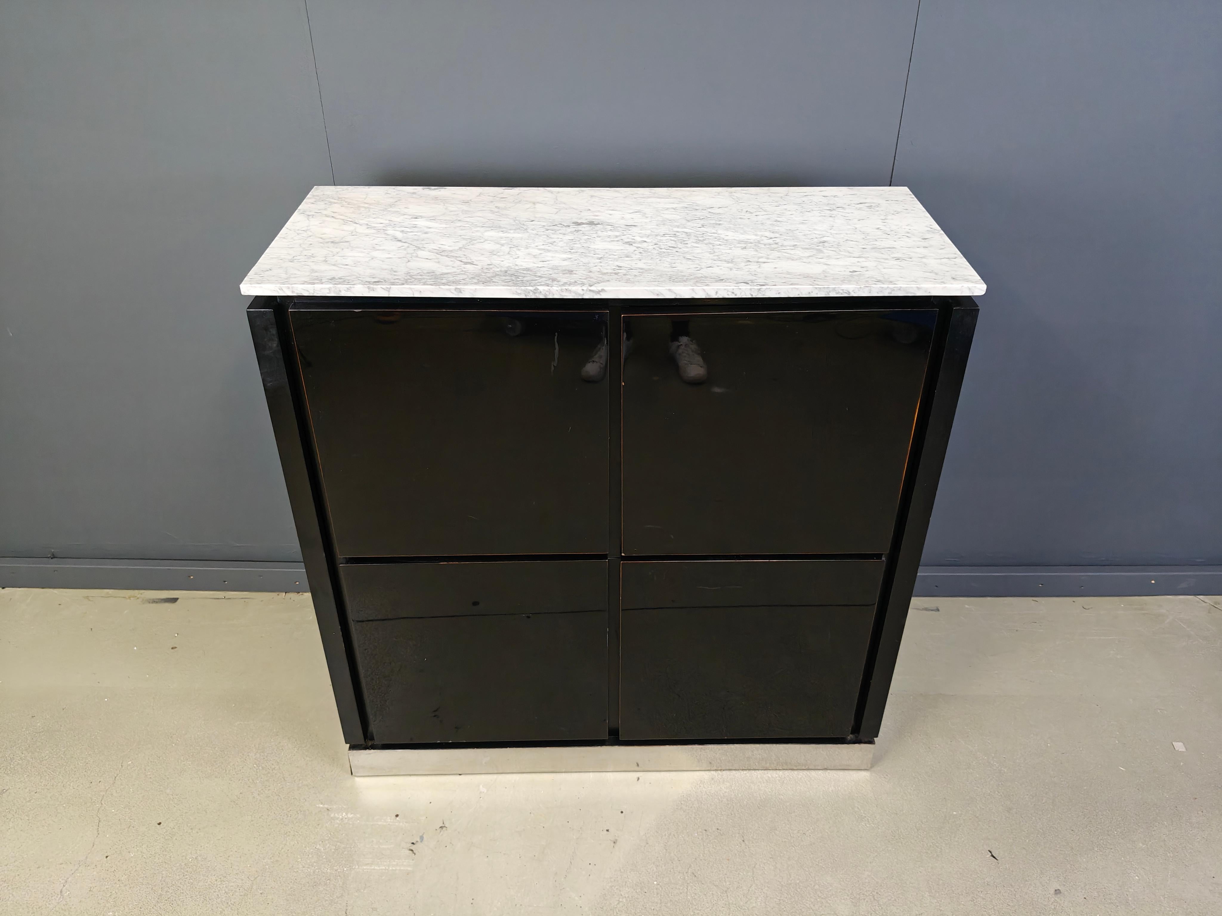 Mobile bar anni '70 con 4 ante laccate nere lucide che rivelano un ampio spazio di archiviazione con ripiano in vetro e portabottiglie.

Bellissimo piano in marmo bianco e piastre metalliche in alluminio sulla base.

anni '70 - Belgio

Presenta un