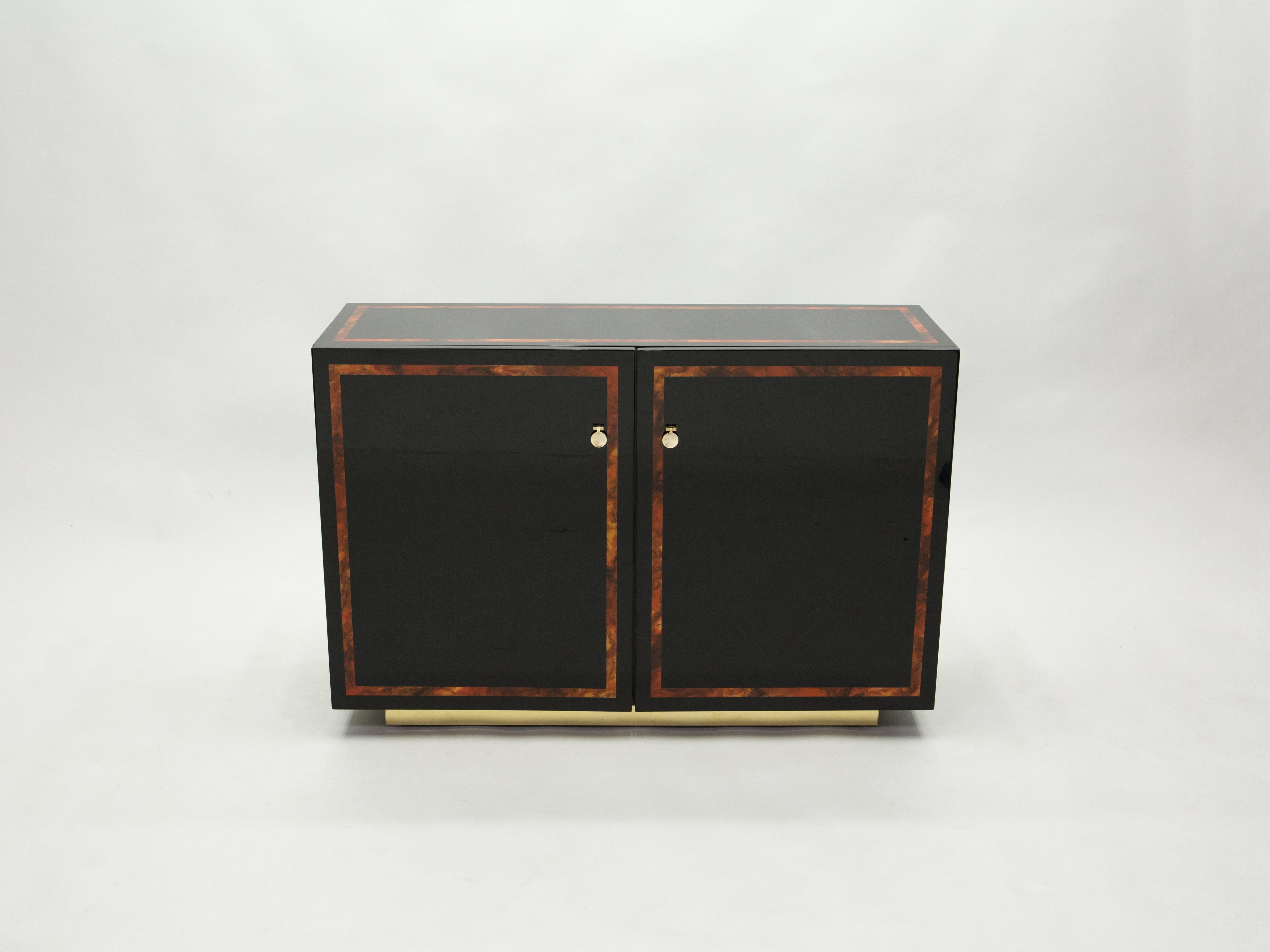 Glossy black lacquer, paired with beautiful burl wood inlay and bright brass accents, feels crisp and luxe on this beautiful sideboard cabinet. Its boxy, simple style is typical of both the 1970s and designer Jean Claude Mahey for Maison Romeo