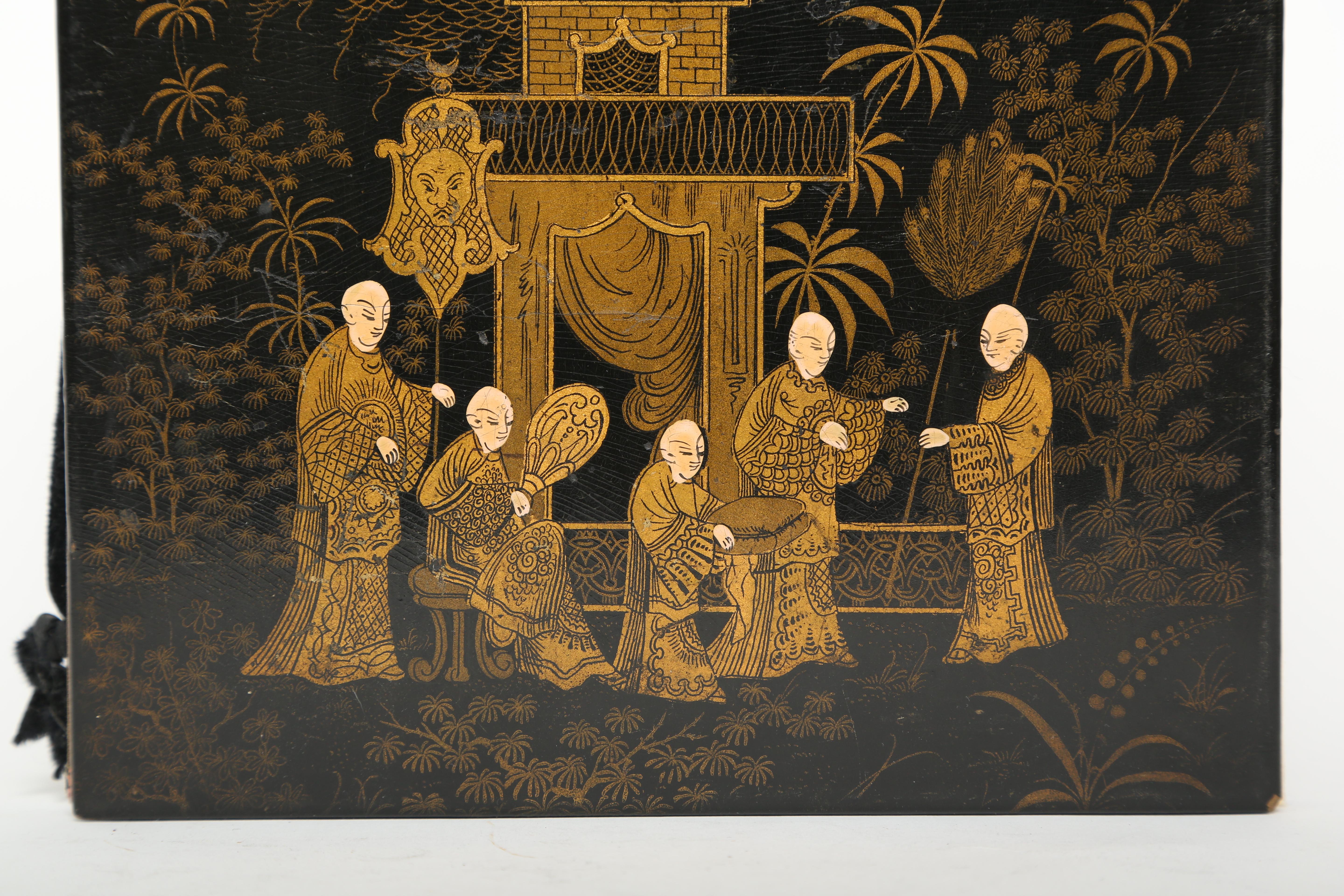 Antique folio or blotter in black lacquer on papier mâché. The scene depicts five Chinese men standing in front of a pagoda with a background of trees and palm trees. One of the men is offering a cushion to the man on the right. The decoration is