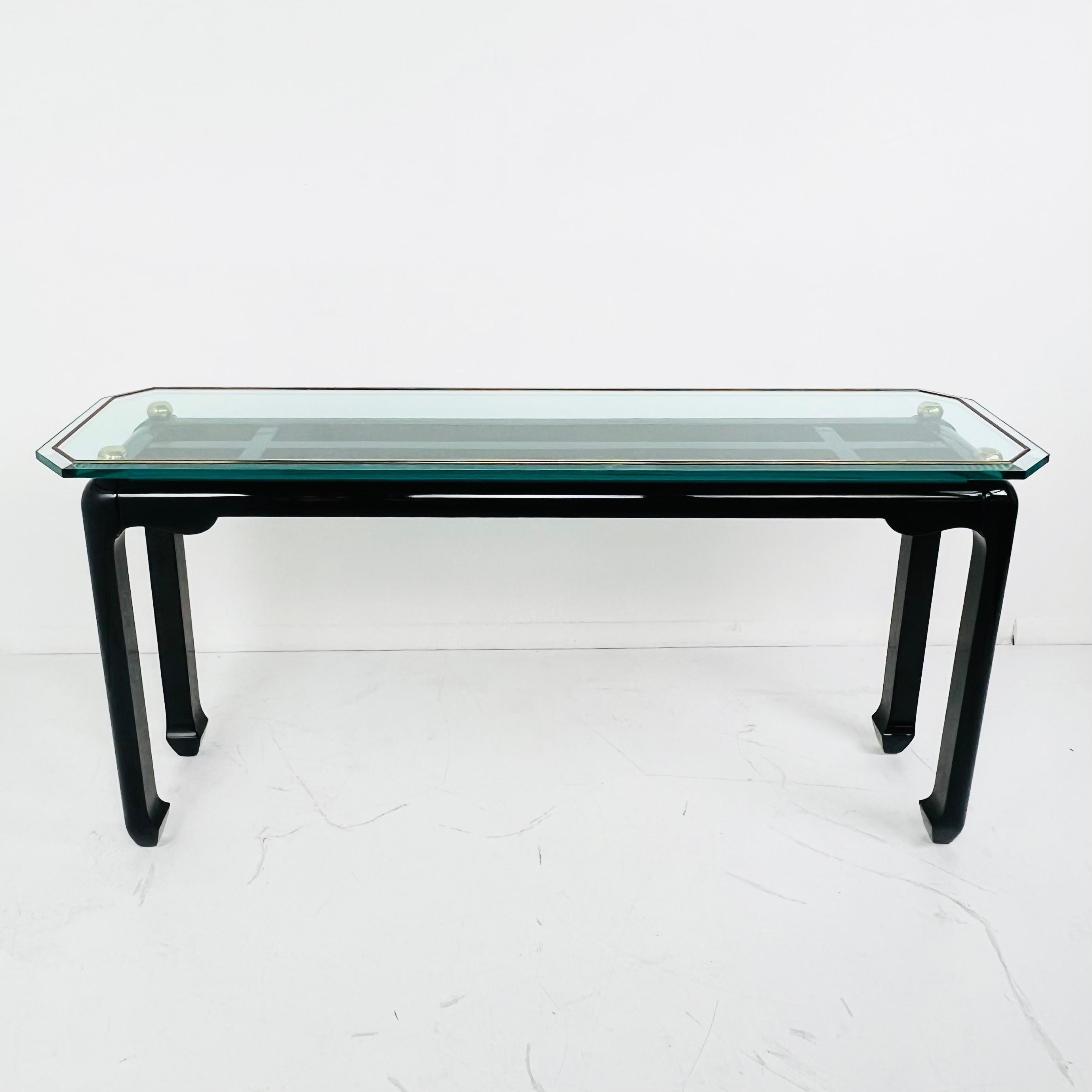 Very handsome console or sofa table in the style of James Mont. Black lacquer Asian style base with brass trim and glass top. Beveled glass top sits on round brass corner finials. Very good vintage condition with some wear (scratches, dings)