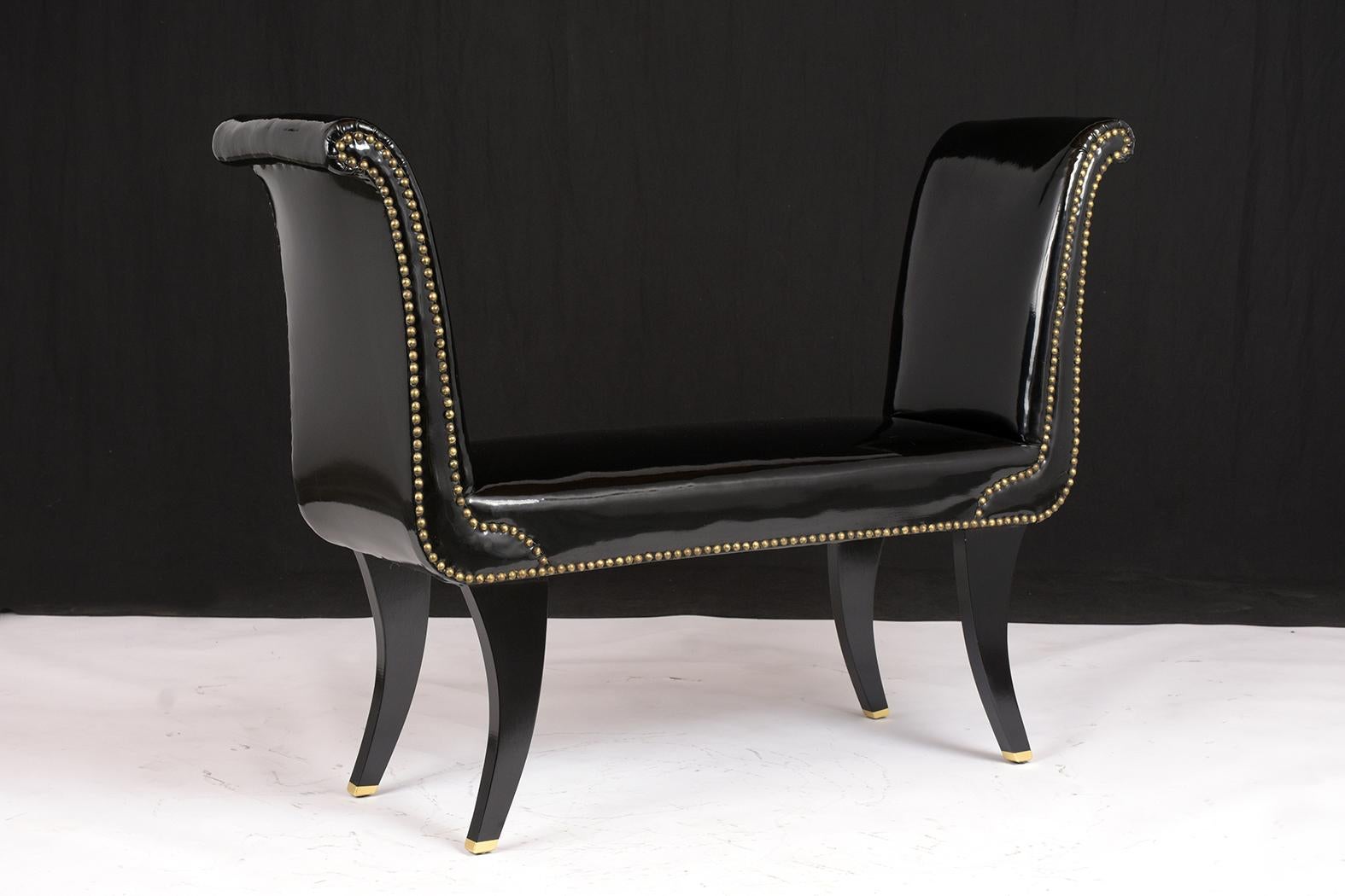 This 1960s Regency Style Bench has been restored and features its original organic black acrylic vinyl upholstery in good condition. The bench also has scroll arms with brass nail trim accents run along the sides. The seat has a coil spring making