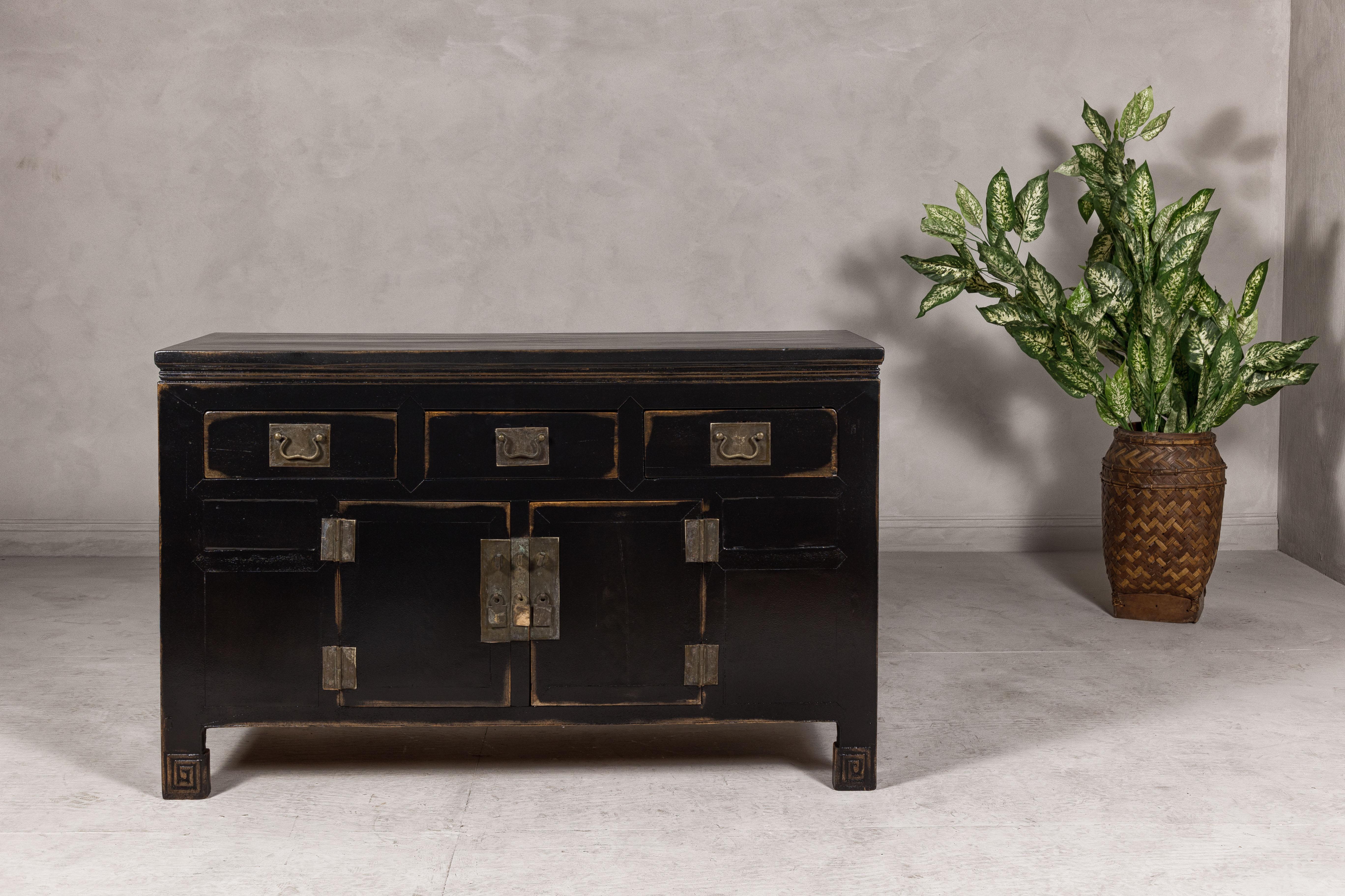 A black lacquered Qing Dynasty sideboard from the 19th century with rubbed edges, brass hardware, three drawers over two doors. This 19th-century Qing Dynasty sideboard exudes timeless elegance with its deep black lacquered finish, thoughtfully
