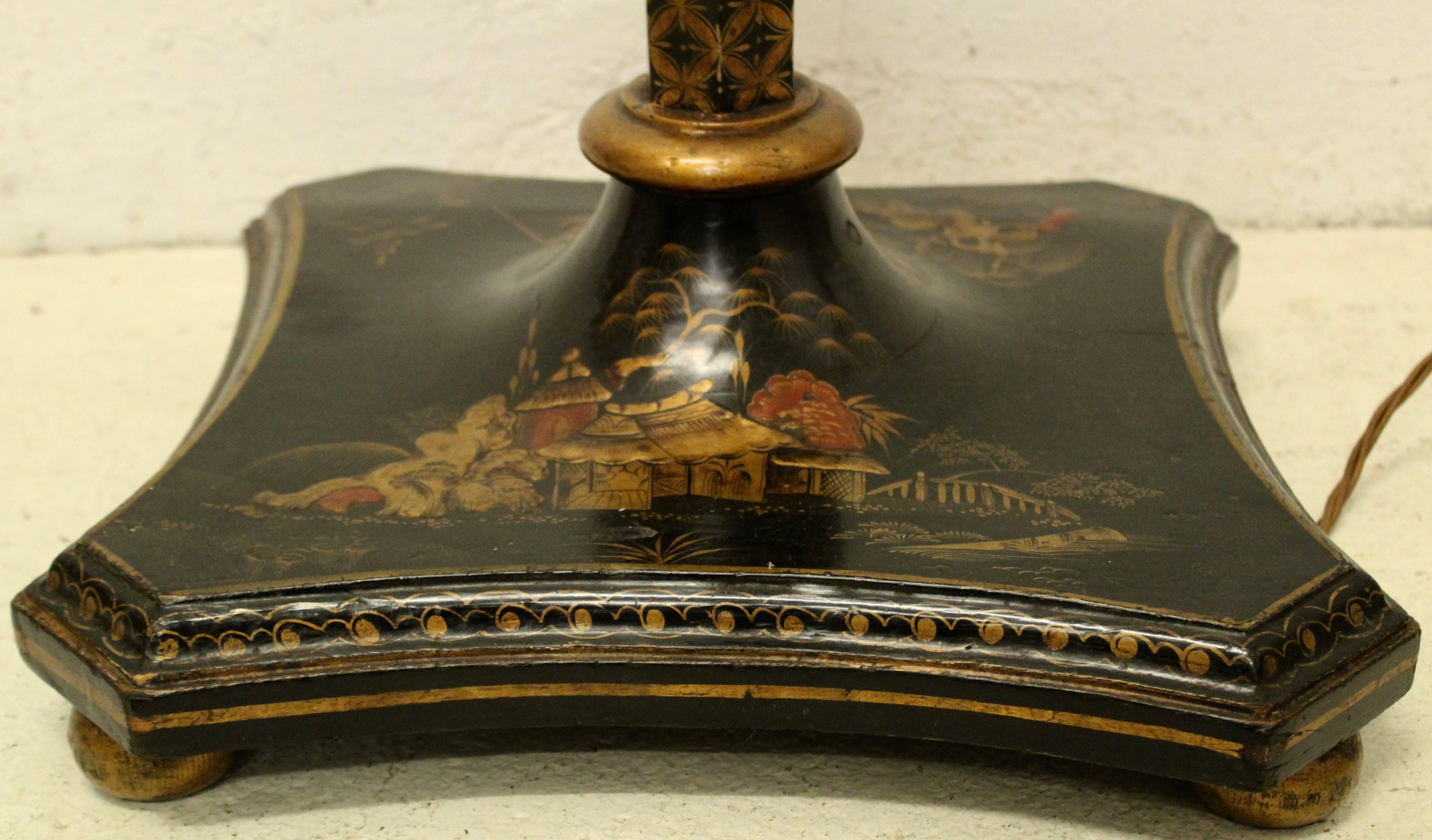 A French chinoiserie standard lamp in black lacquer, circa 1950. The shaped base, supported by giltwood squashed bun feet, decorated with red and gilt detailing depicting pagodas and landscape scenes. The hexagonal column, interspersed with gold and