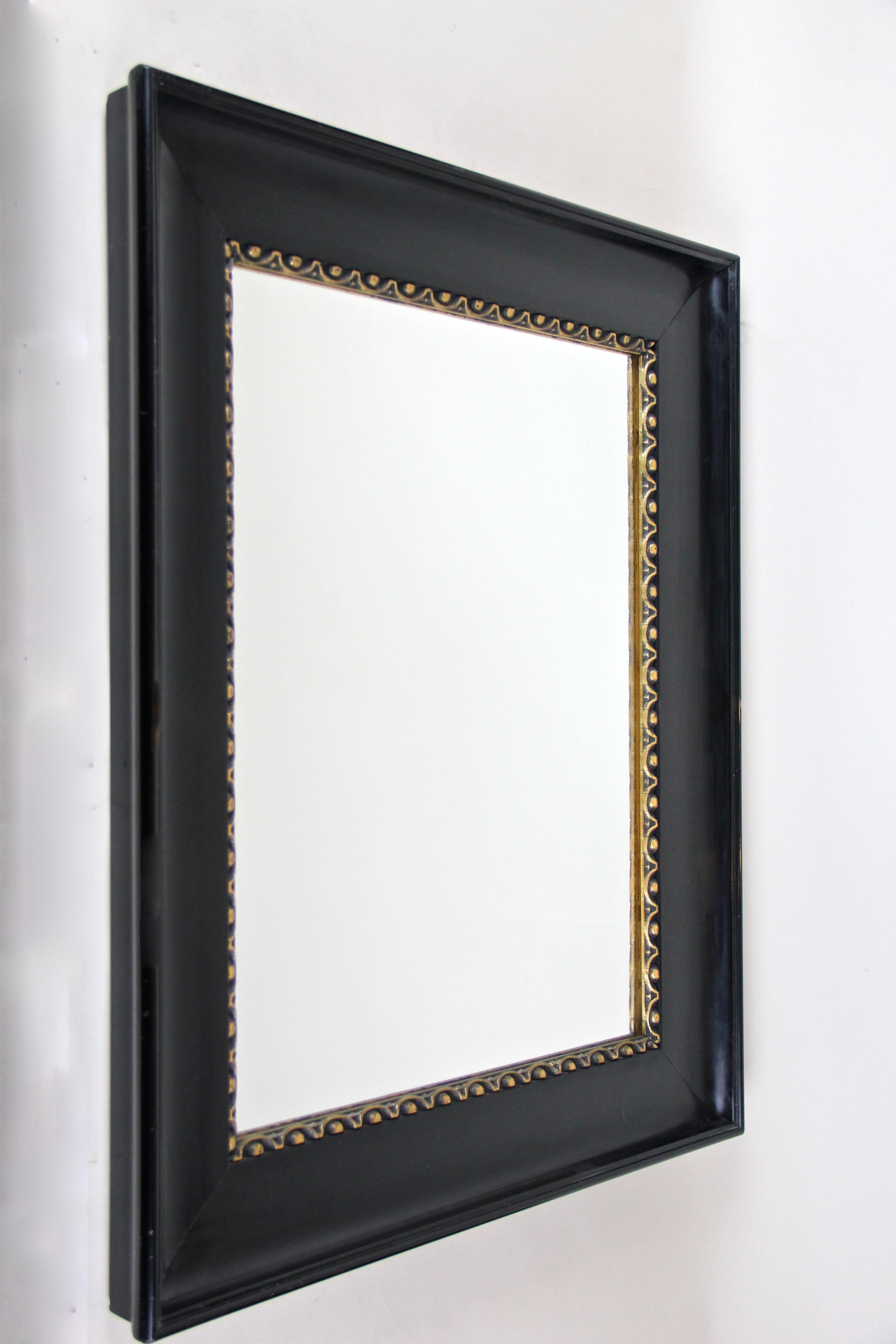 Delightful black lacquer wall mirror with gilt bars from circa 1900 in Austria. The pleasant black lacquered mirror shows a broad, chamfered glossy frame adorned by beautiful designed gilt stripes on the inside. Famous for the very early 20th