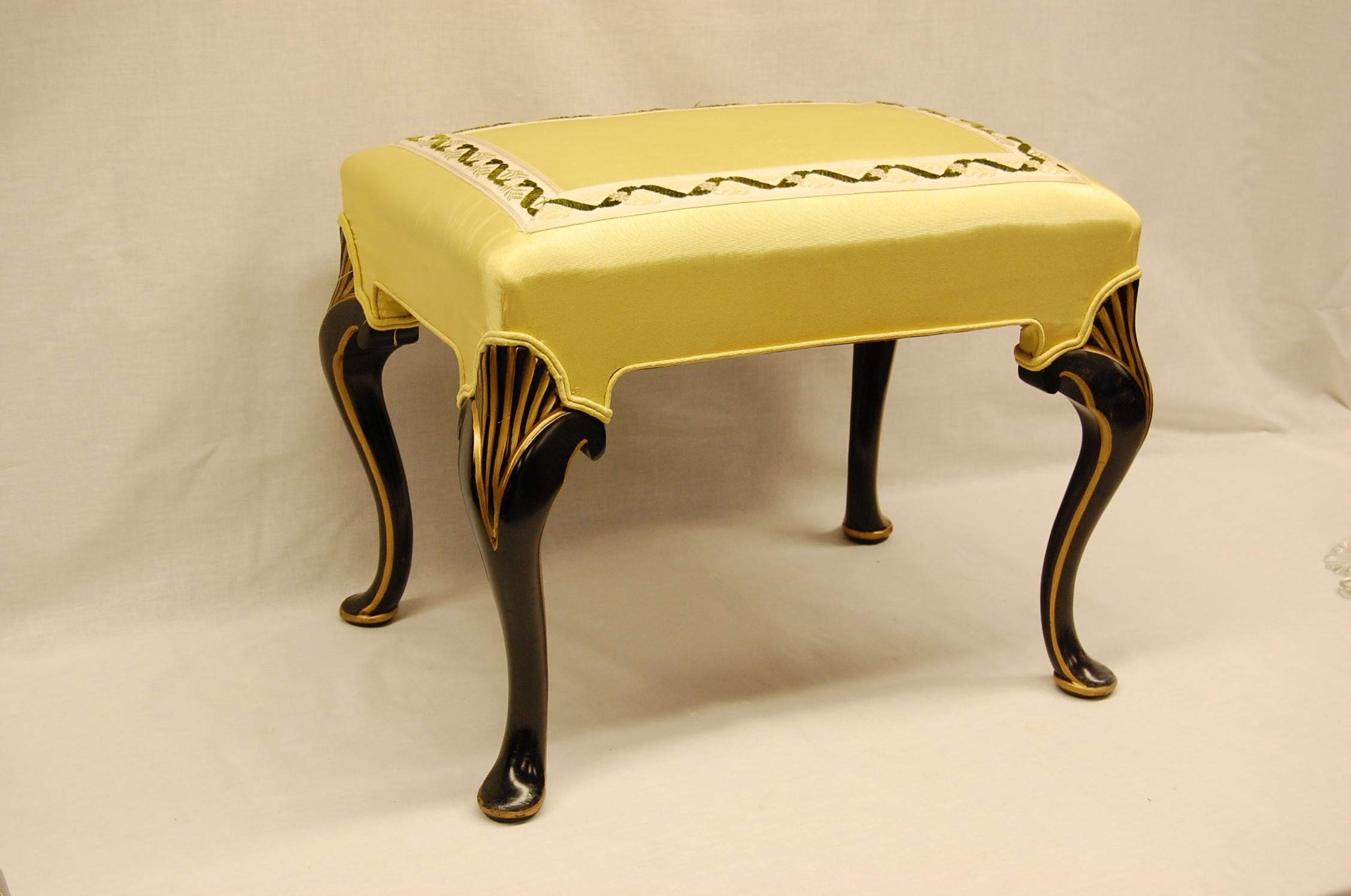 Bench in excellent condition covered in yellow moire fabric with braid on the top surface. Black painted legs with gold accents.