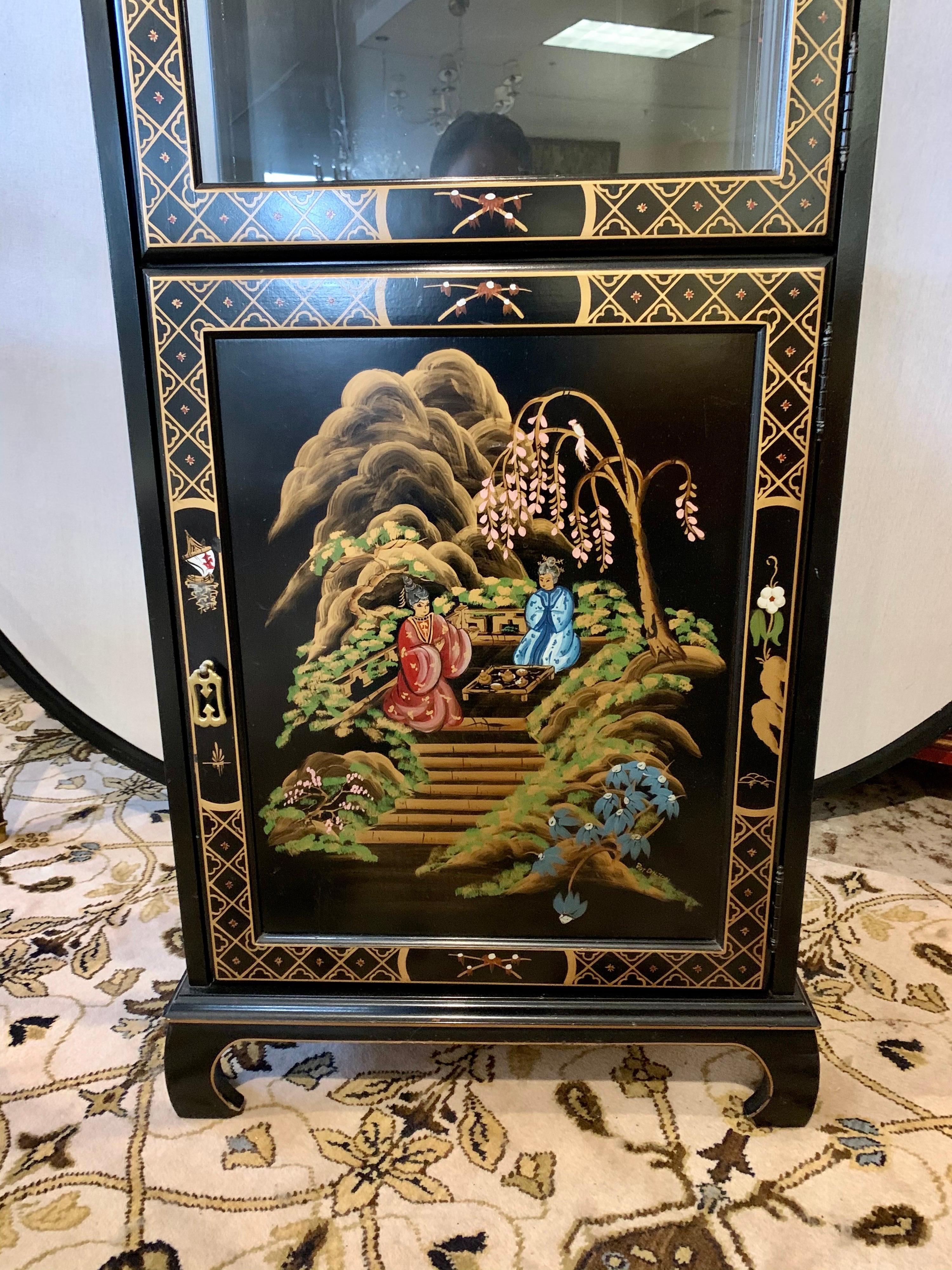 Vintage black lacquer chinoiserie vitrine display cabinet with beautiful hand painted scenery on three sides. It has glass on the top front doors and sides. The front doors open to glass shelves which are illuminated from above. The bottom portion