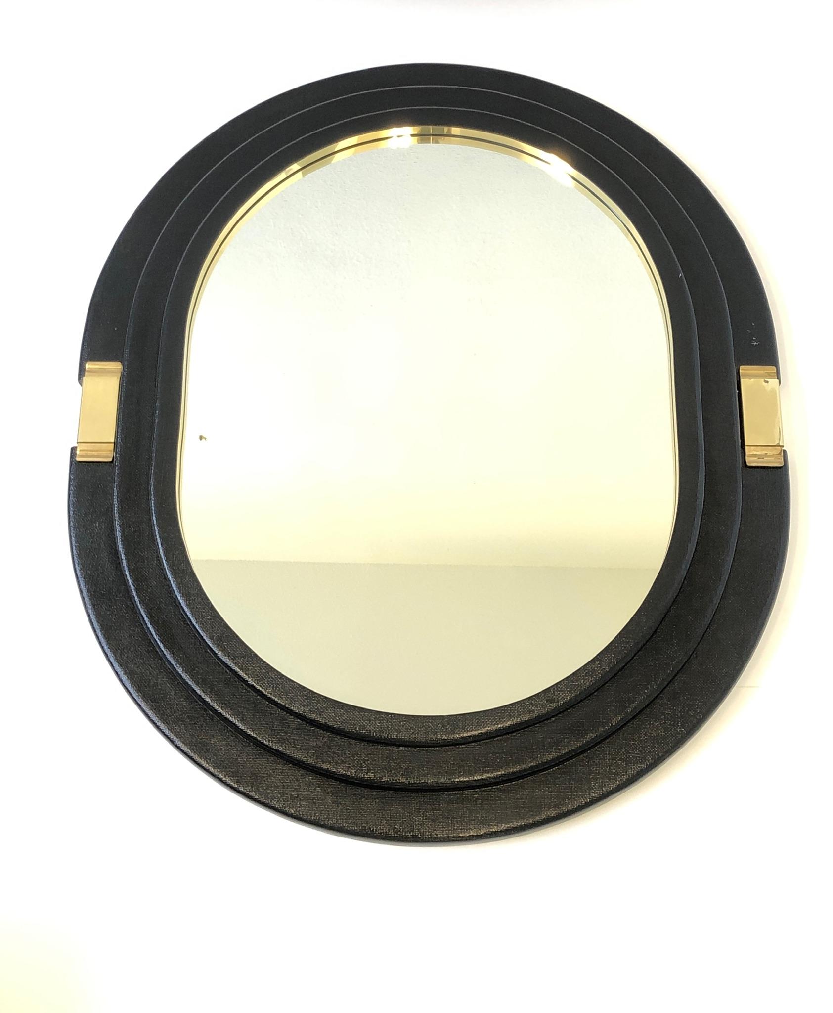 A glamorous black lacquered Linen and polished brass oval mirror from the 1980’s. The frame is constructed of wood wrapped in linen and black lacquered with polished brass details. 

Measurements: 39” wide, 46.5” high and 3.25” deep.