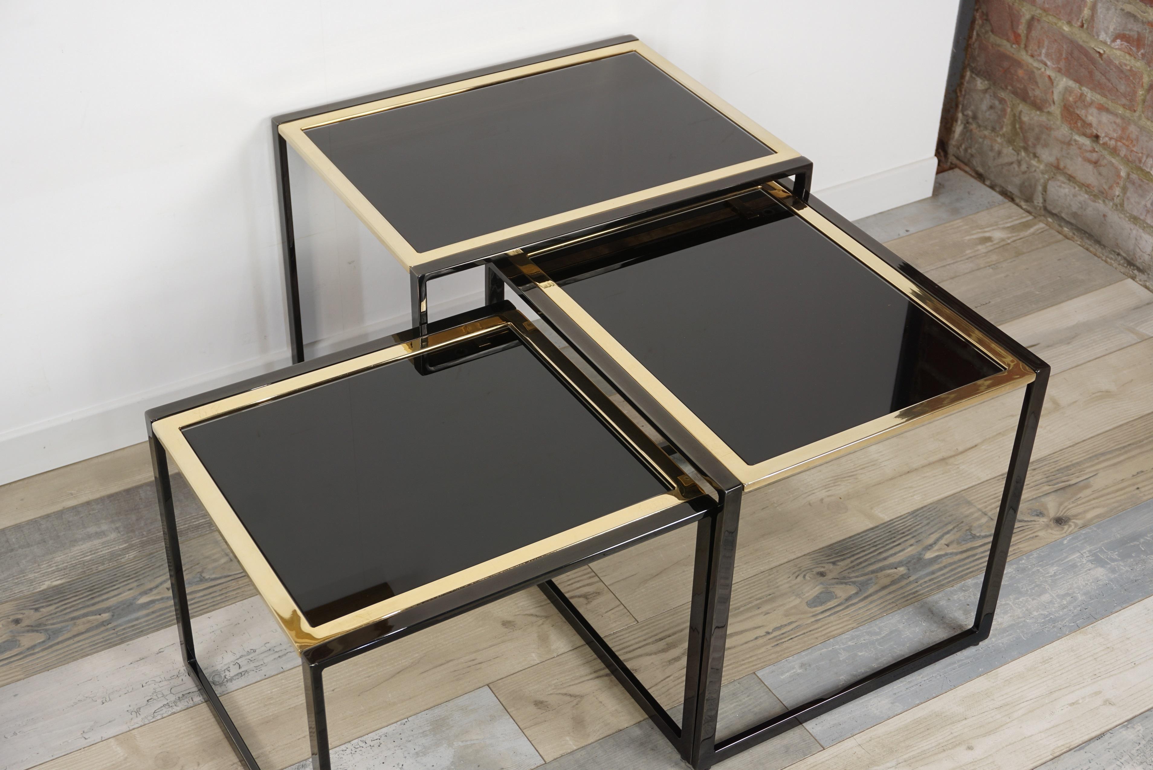 Set of nesting tables reminiscent of the work of Roger Vanhevel in the 70s: black lacquered metal structure with gold-plated finish, sled base, mirrored and glass trays. Beautiful, sumptuous and brilliant, a set of exception, charm and character in