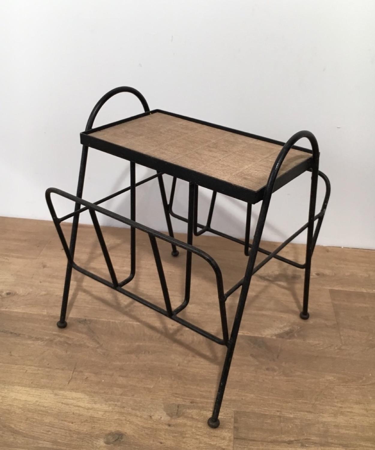 This magazine rack is made of a design black lacquered metal base with a rattan shelf. This is a French work, circa 1950.