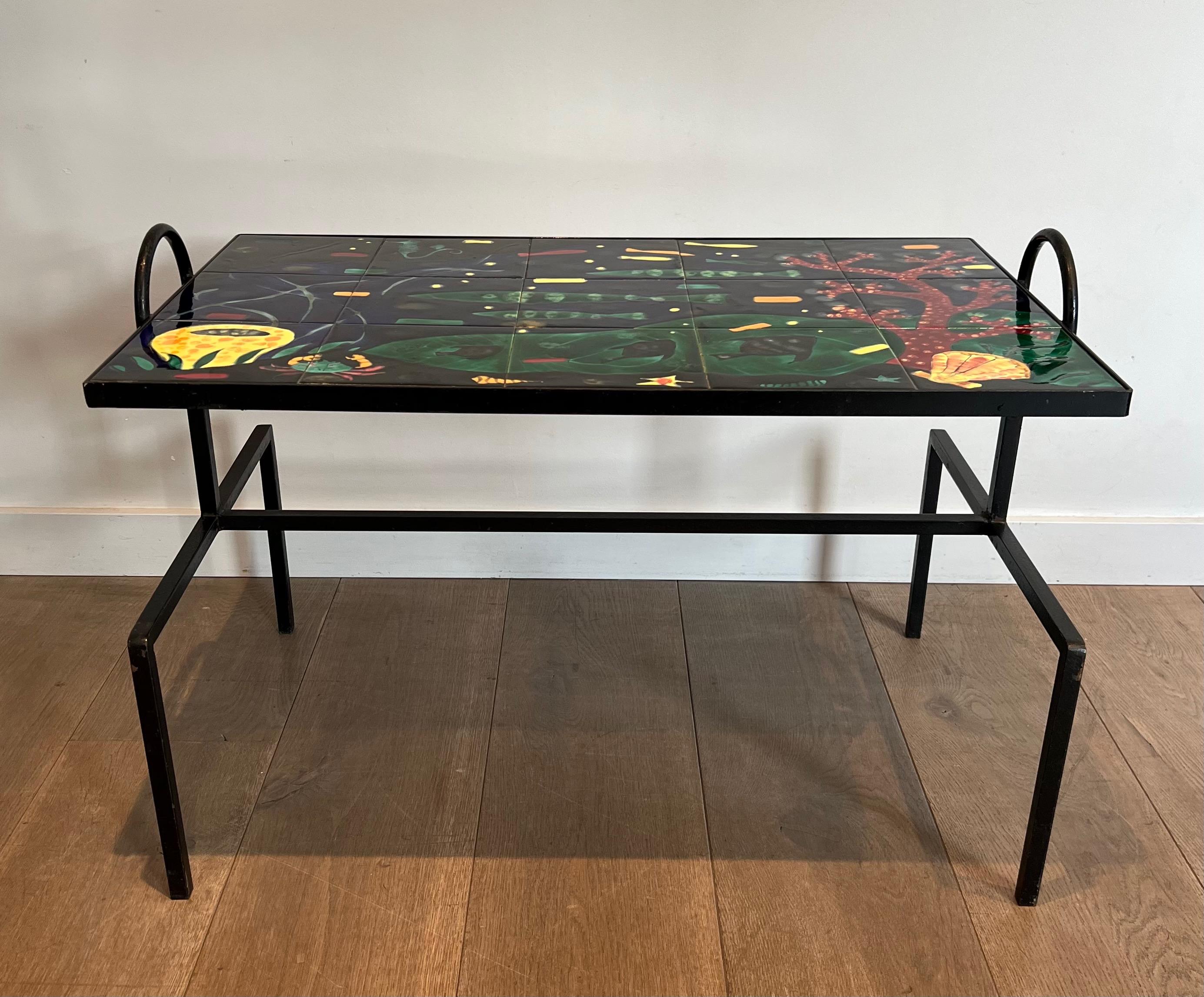 Cette belle table basse design est composée d'une base en métal laqué noir avec des carreaux de céramique décorés de poissons et de coraux stylisés. Il s'agit d'une œuvre française dans le style du célèbre designer Jacques Adnet. Circa 1950