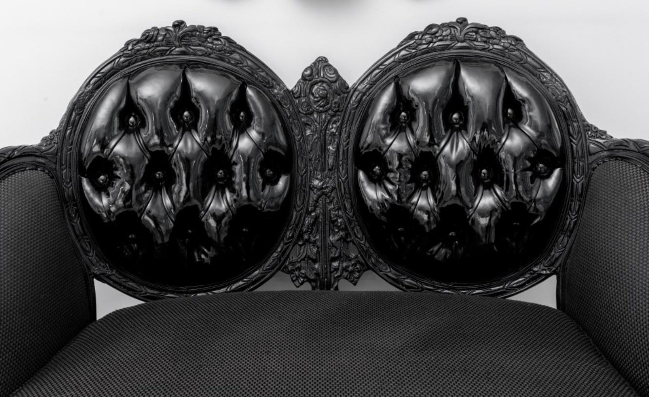 Causeuse en bois noir sculpté de style transitionnel Louis XV-XVI, néo-Napoléon III, reposant sur des pieds cabriole, assise et accoudoirs garnis de tissu noir, dossier garni de vinyle boutonné. 36