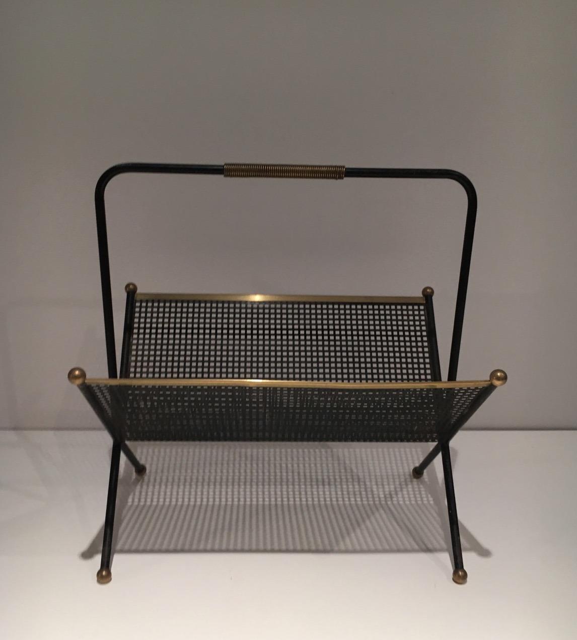 This magazine rack is made of a black lacquered perforated sheet with brass elements. This is a French work. Circa 1950.