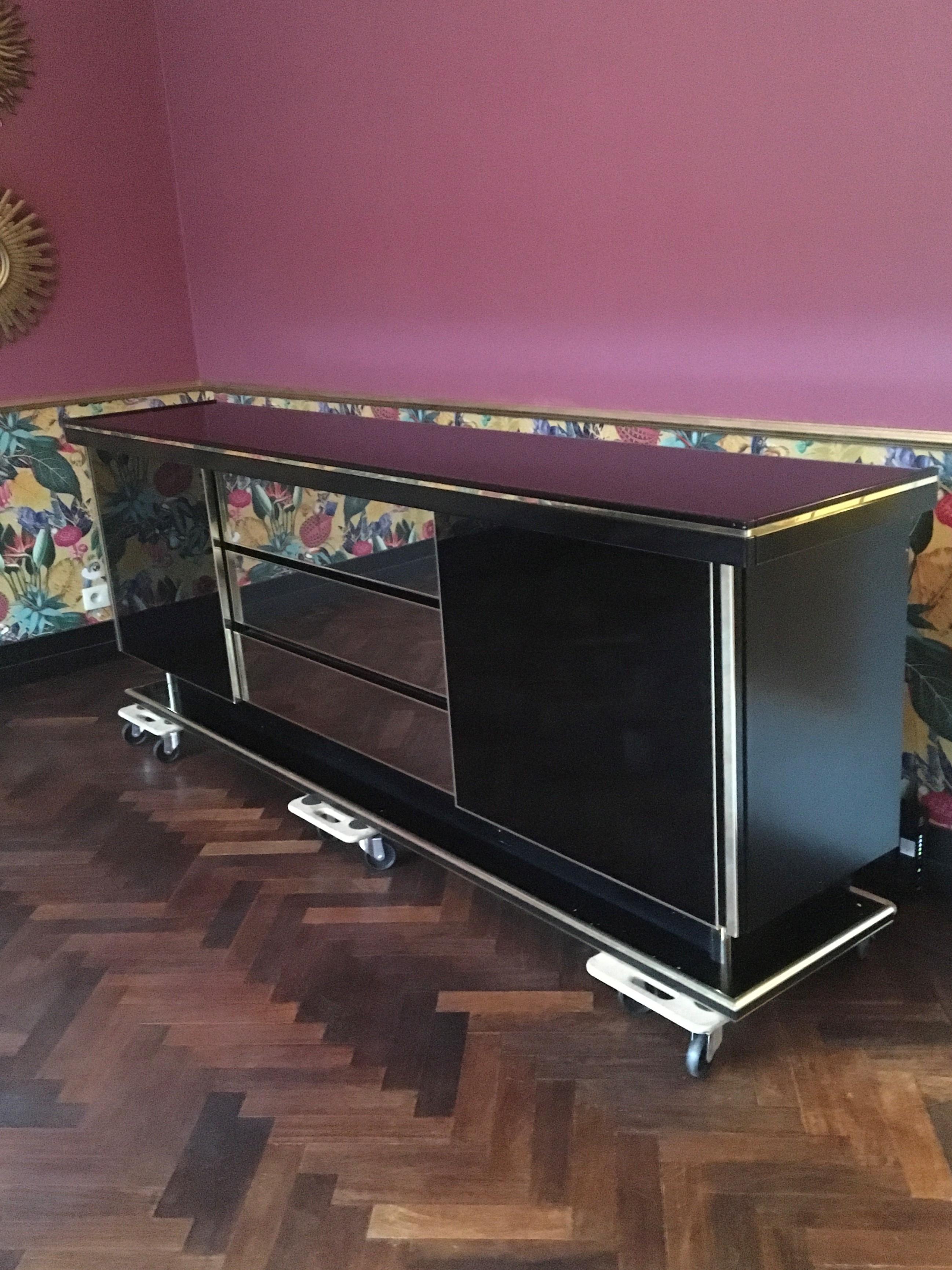 Stylish black lacquered sideboard. 
This European sideboard or credenza is made of black lacquered wood with beautiful golden details and a black acrylic top. Left and right 2 sliding doors with shelves inside and in the middle 3 mirrored drawers.