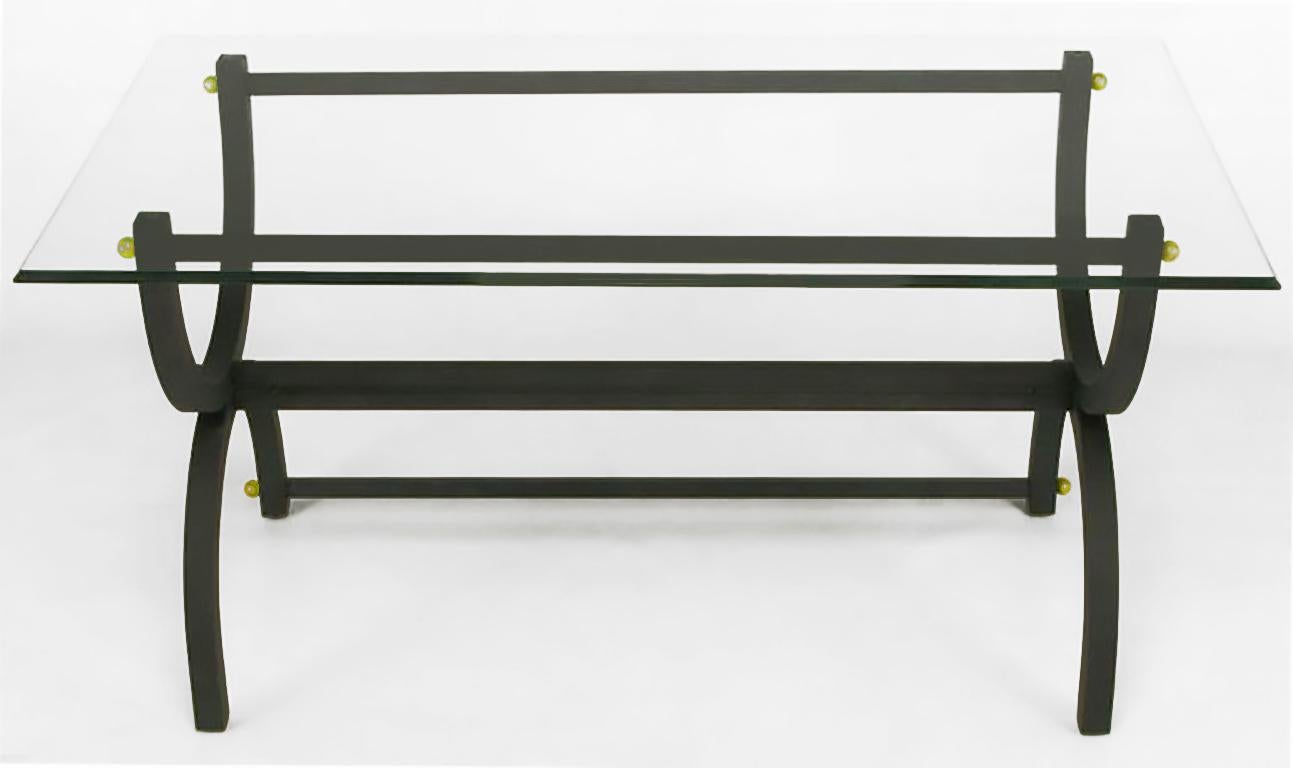 Matte black lacquered steel curule form writing table, with lower back stretcher and multiple brass ball details. Triple beveled ogee edge glass top is one-half inch thick. With a narrower glass top, would also function as a console or sofa table.
 