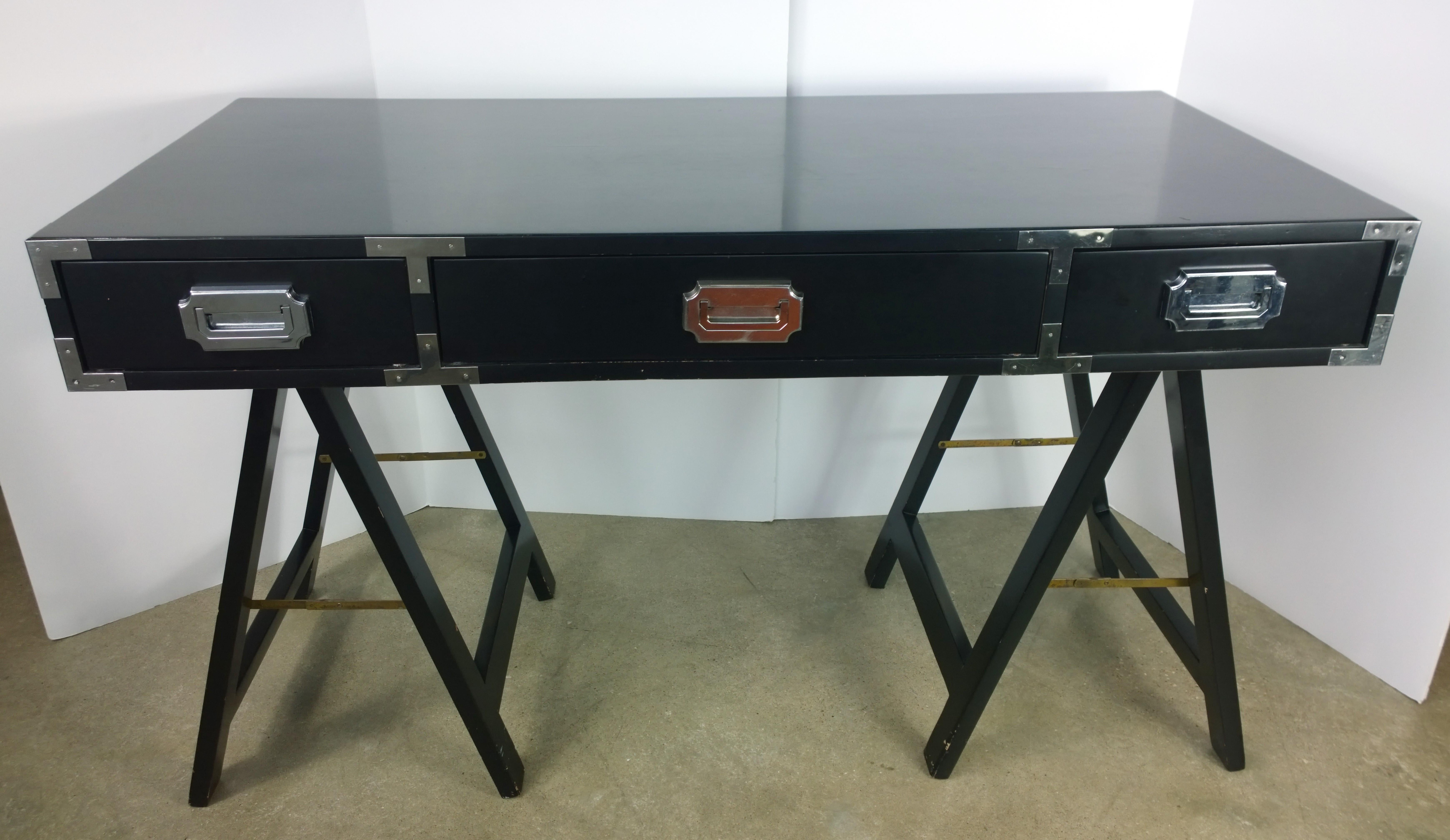 Offered is a Mid-Century Modern lacquered in black, three-drawer Campaign style desk or writing table with chrome and brass accents. The black lacquered Campaign desk with chrome pulls has special grooves that enables the top to sit securely upon
