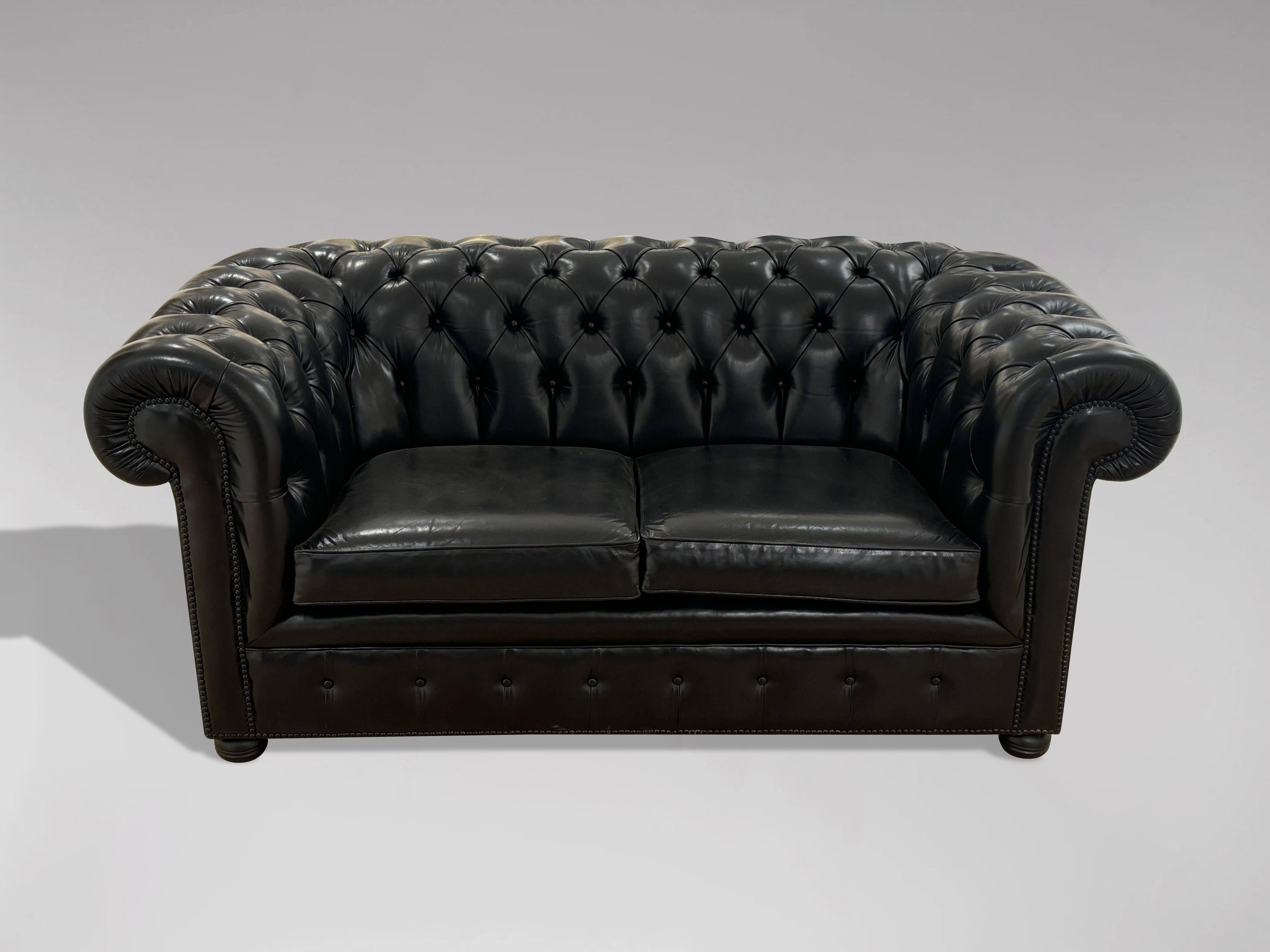 Chesterfield à deux places en cuir noir de bonne qualité du 20e siècle, avec deux coussins détachés, reposant sur des pieds en chignon ébonisés. Avec garniture en laiton cloutée individuellement à la main. Un bel exemple de chesterfield confortable