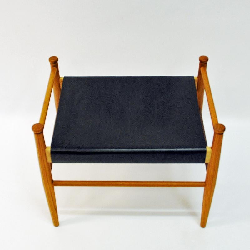 A lovely teak and black leather taburette Sudan by Gillis Lundgren for Ikea Möbler in the 1960s, Sweden. Practical in every occasion both as an extra chair or a foot stool for your legs. Rounded and decorated teak knobs on the sides. Rope attachment
