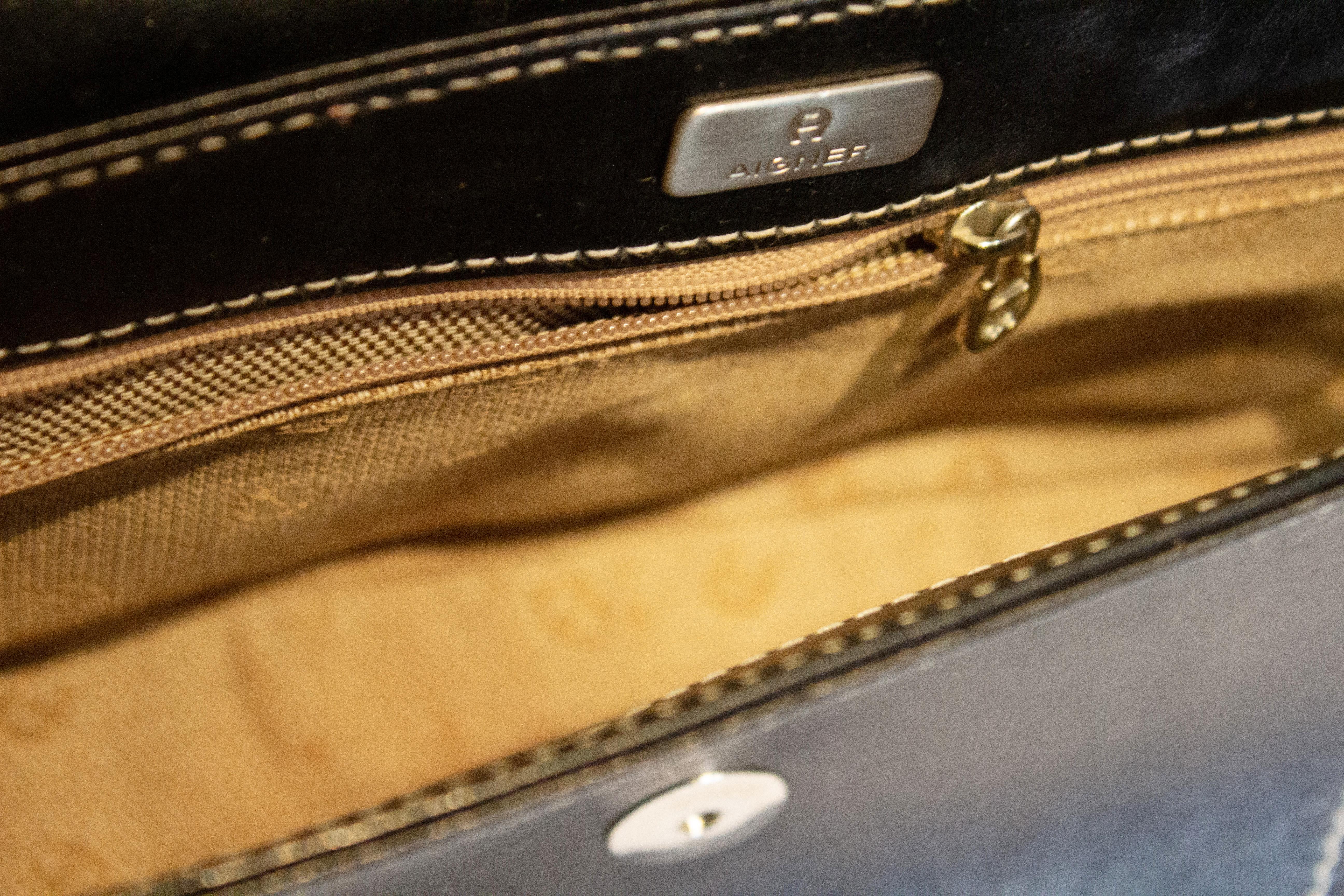Un sac chic en cuir noir signé Etienne Aigner. Le sac est en cuir noir avec des surpiqûres blanches, possède un rabat sur le devant et une poche intérieure zippée.  
Dimensions : largeur 12'', hauteur 6'', profondeur 2 1/2''.