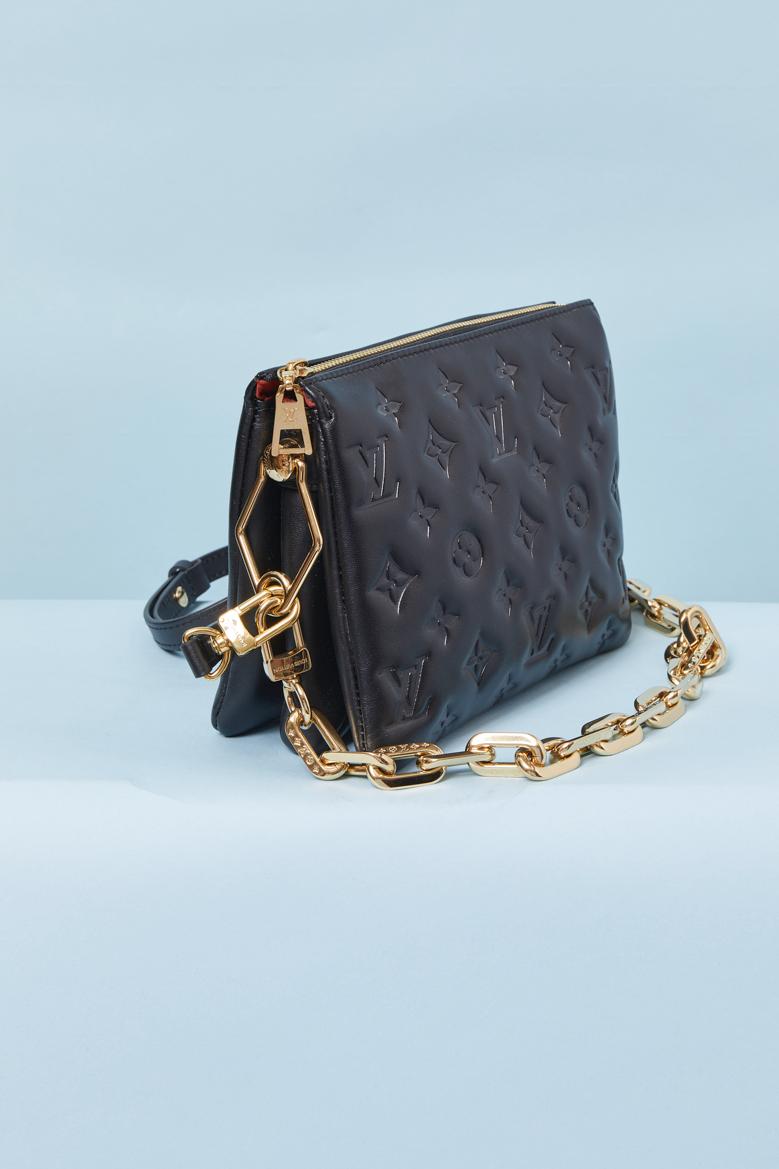 Borsa in pelle nera con monogramma in rilievo e doppia tracolla, una in catena di metallo dorato e una in pelle staccabile. Fodera in pelle scamosciata arancione. Chiusura con zip sul davanti con tirazip del marchio. Una tasca interna con zip.